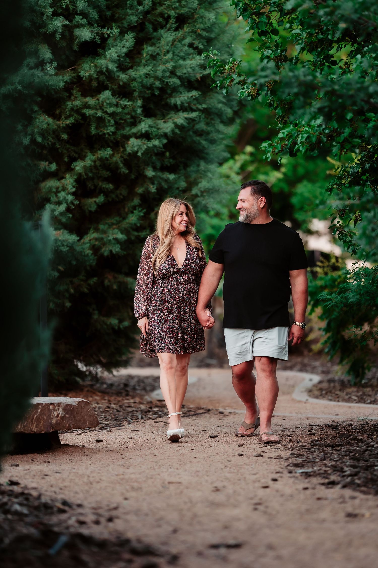 A romantic couple walking hand in hand along a scenic dirt trail surrounded by lush greenery.