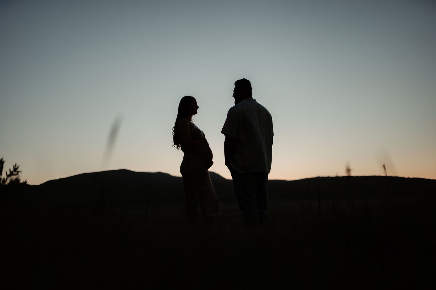 Two silhouettes stand together on a hilltop in a romantic sunset composition.