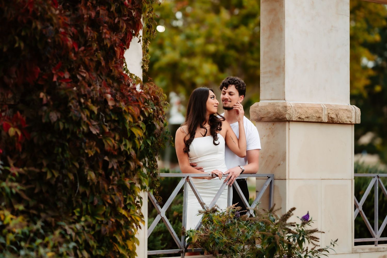 A couple shares an intimate moment together on a garden terrace surrounded by autumn foliage.