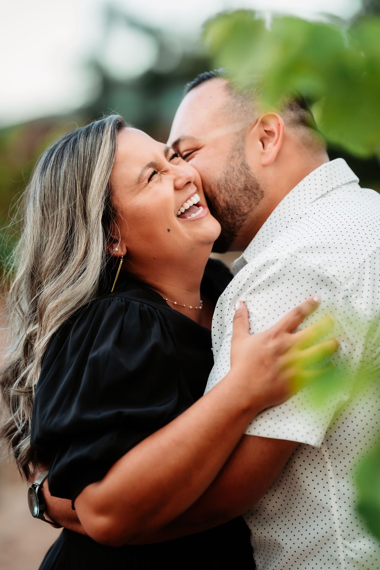 A romantic couple embraces and shares tender kisses in a series of candid outdoor photos with green foliage in background.