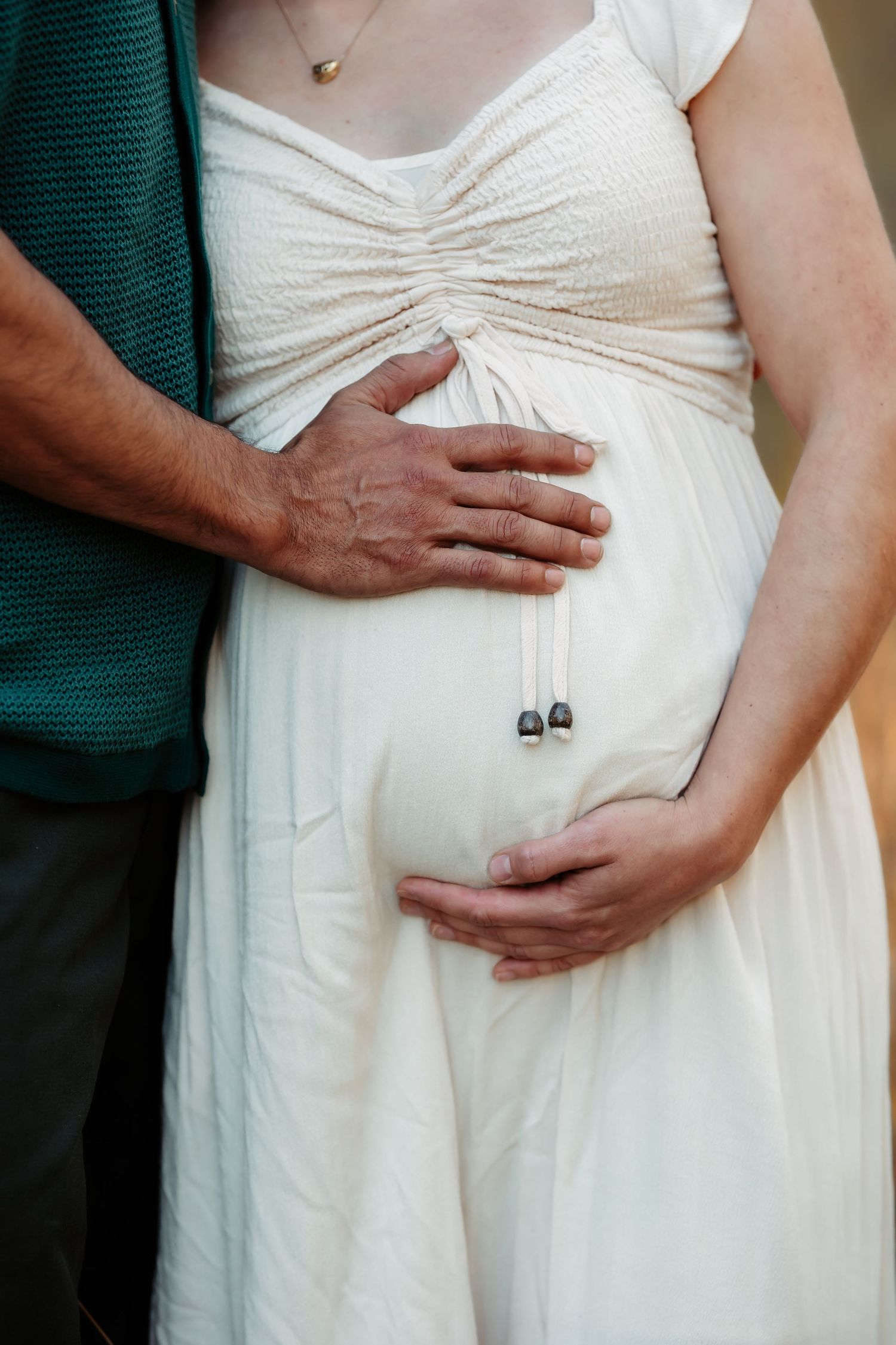 Close-up series showing hands gently cradling a white-dressed figure's midsection in an intimate maternity pose.
