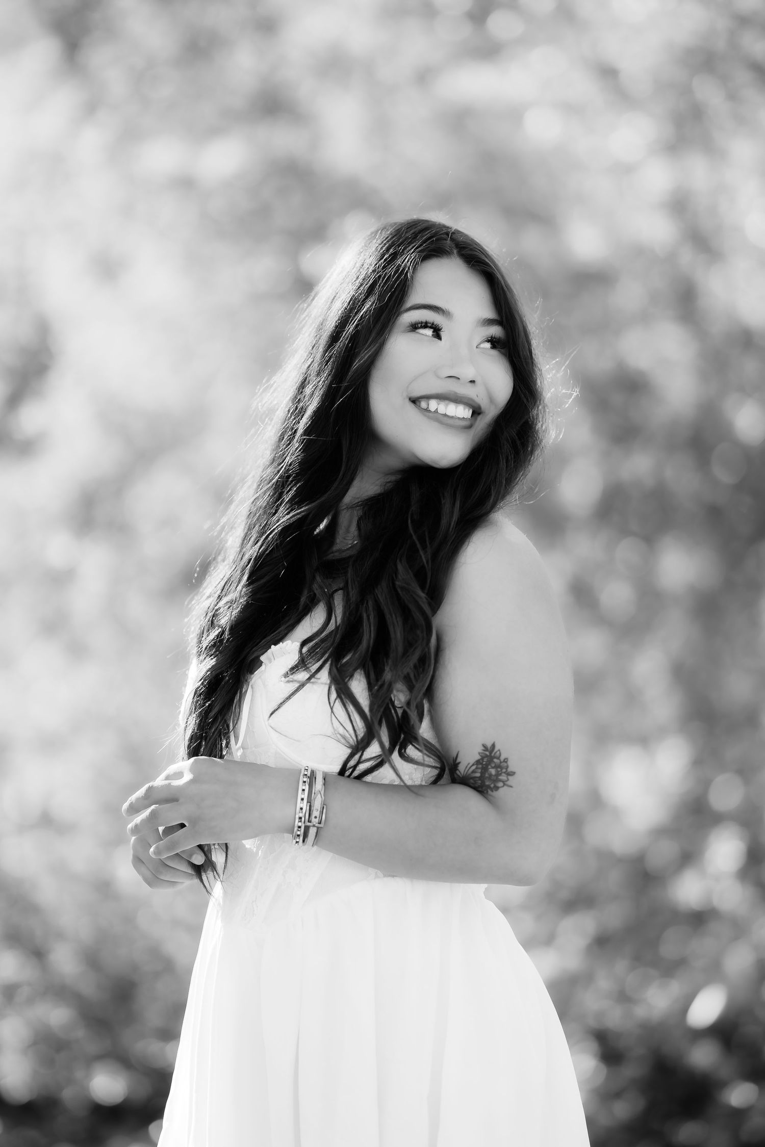 Black and white portrait of graduate in white dress with soft bokeh background.