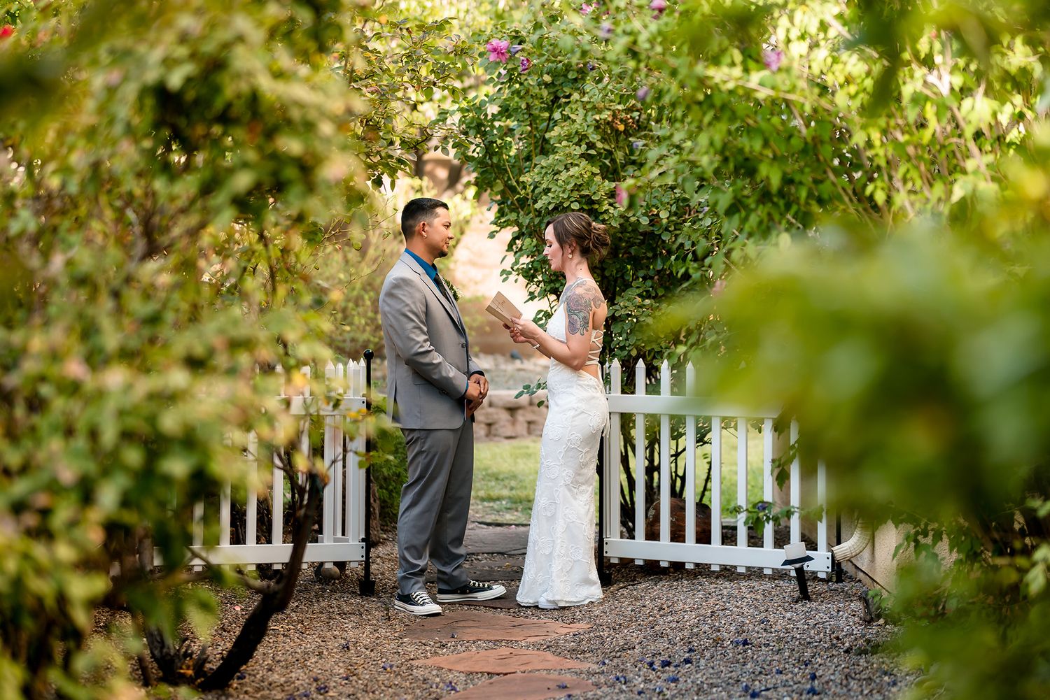 Bride and groom exchange vows in a lush garden ceremony beside a white picket fence.