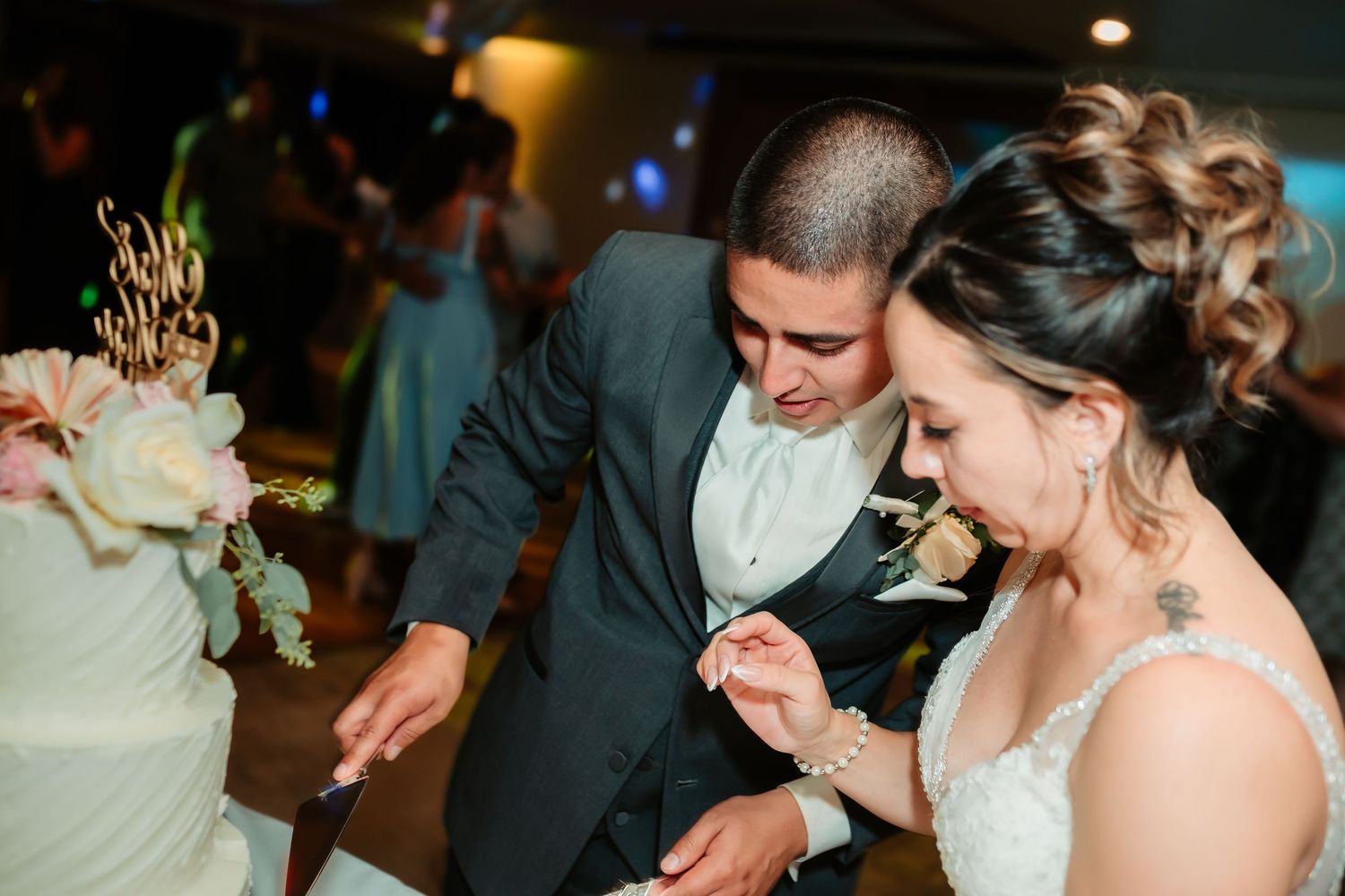 A couple shares a playful moment while cutting their wedding cake at the reception.