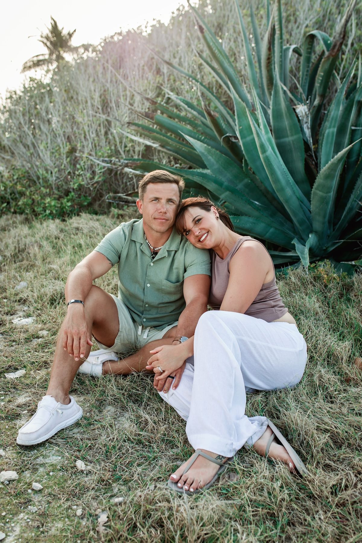 A couple sitting together on grass near a large agave plant during golden hour lighting.
