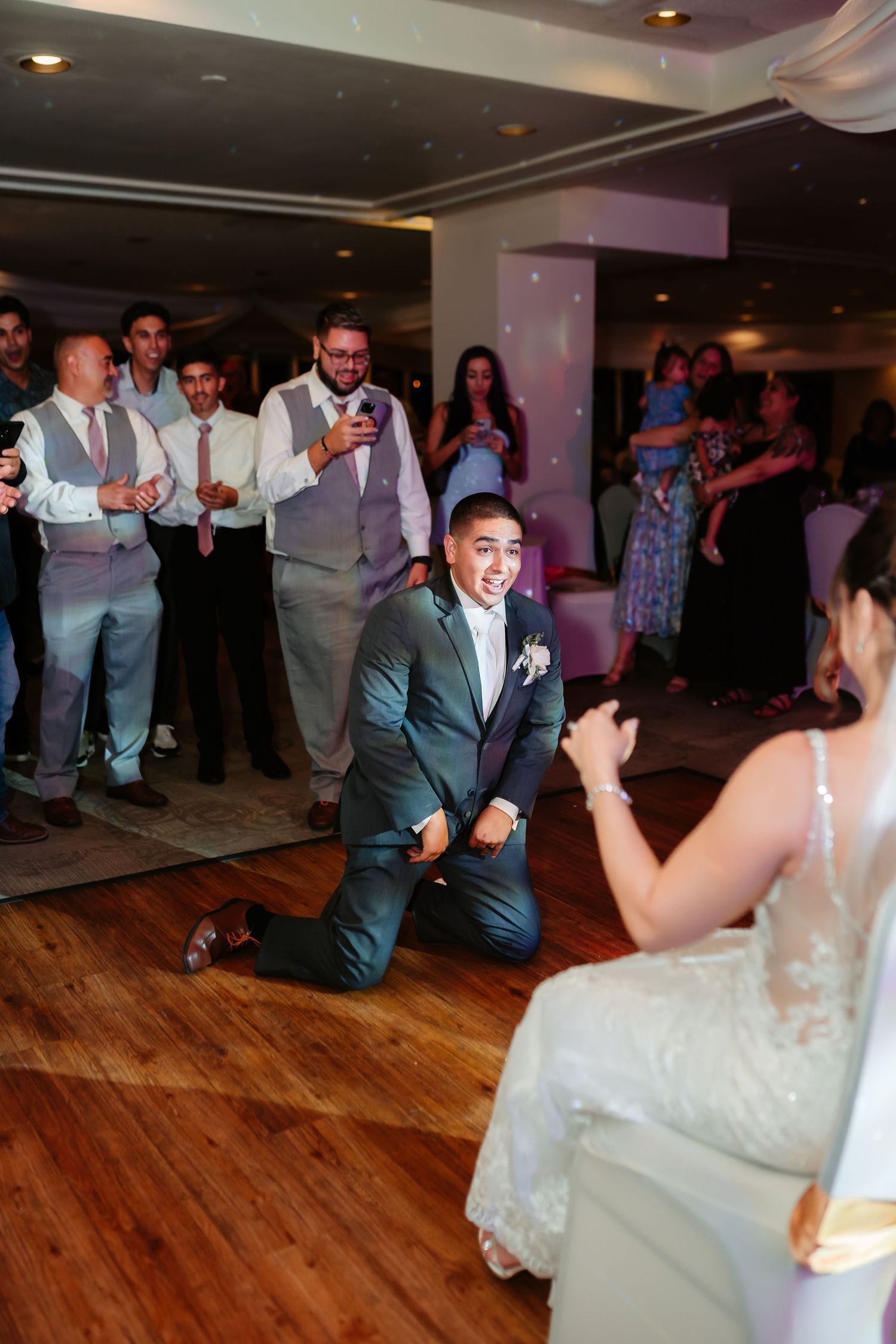 Wedding couple performs choreographed dance moves on wooden floor under pink lighting.