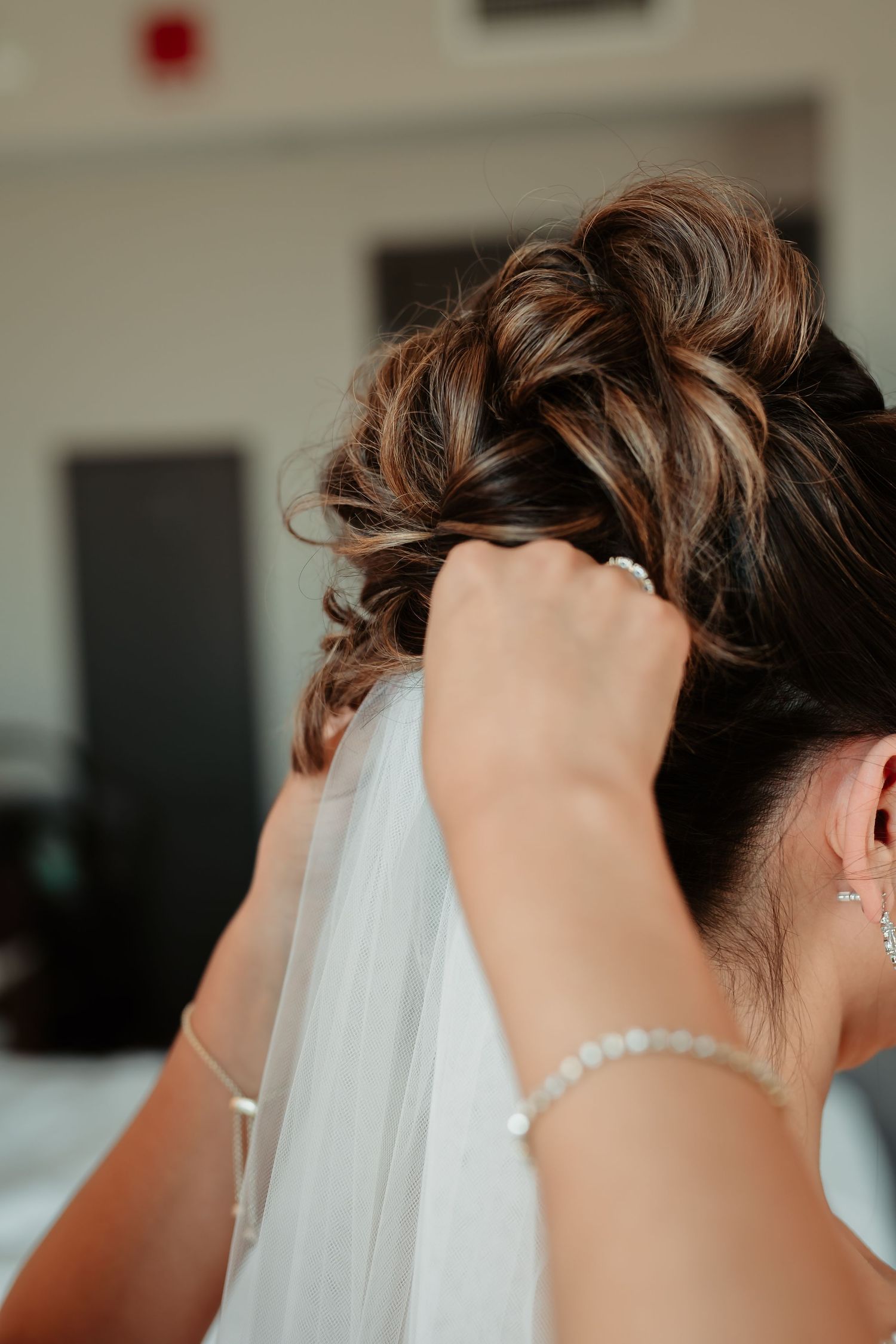 Side profile view of an elegant bridal hairstyle with a white veil and pearl drop earrings in a candid moment.
