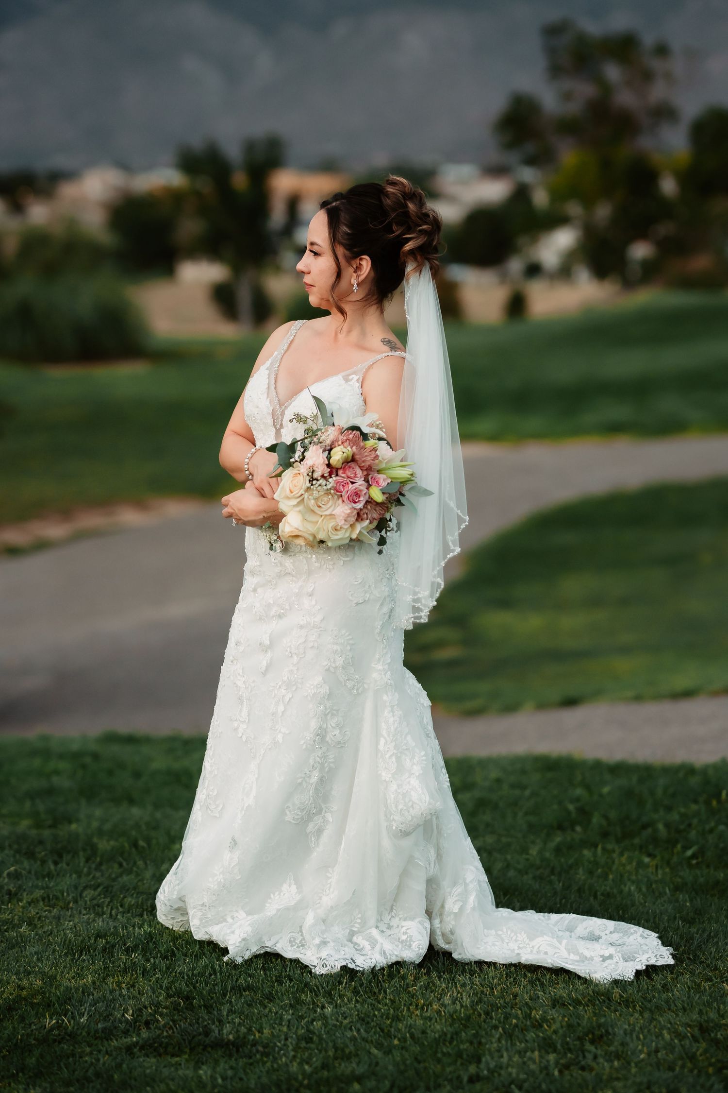 Bride in lace wedding dress walking on grass with mountain backdrop.