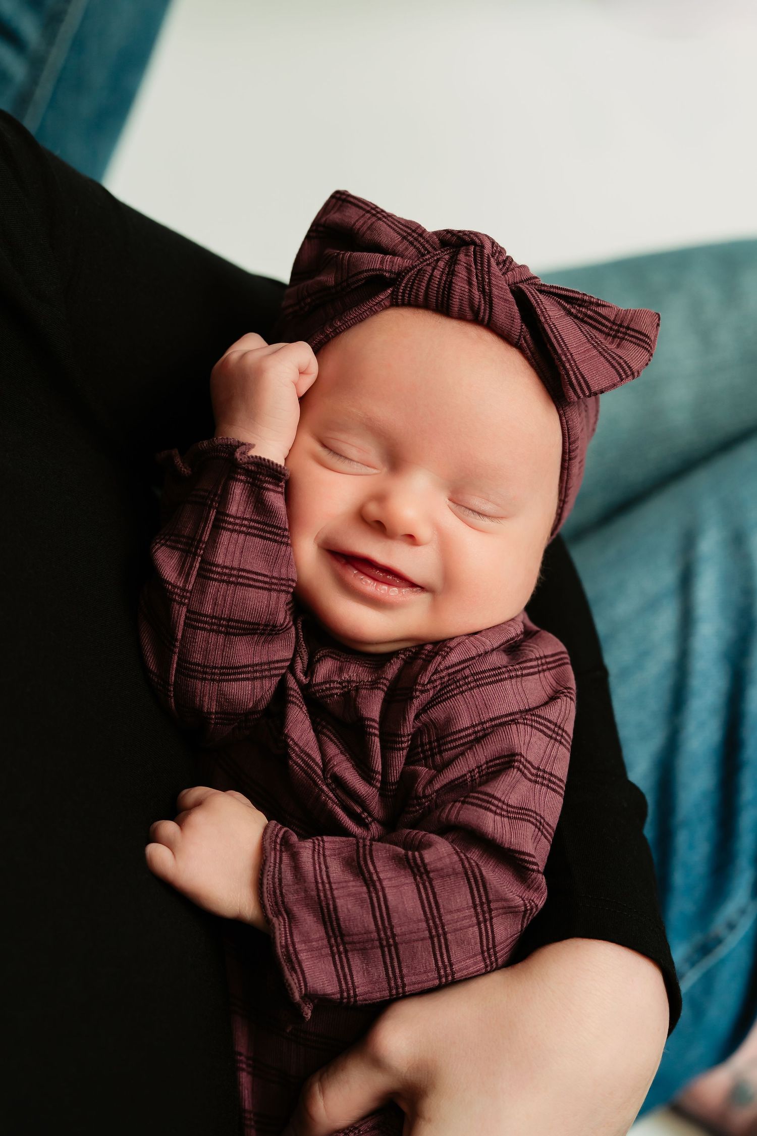 Sleeping newborn in burgundy plaid outfit with bow rests peacefully on teal blanket in series of closeup portraits.