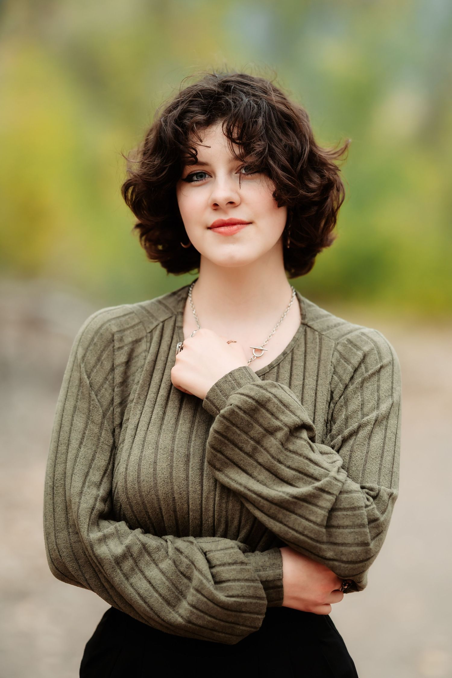 A person in a chunky olive green knit sweater poses against a blurred outdoor background.