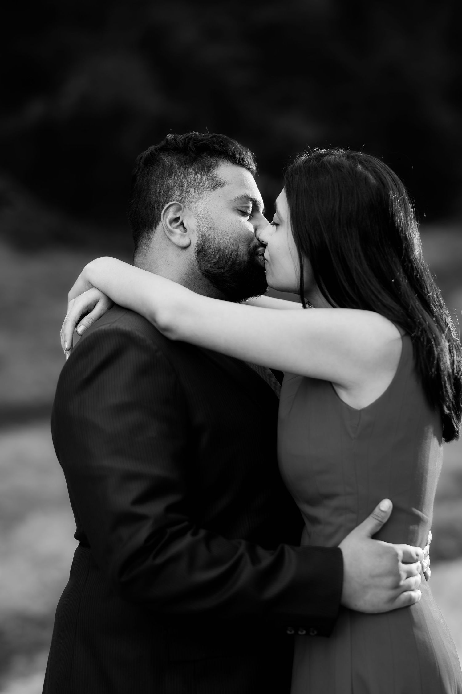 Intimate black and white portrait of couple sharing romantic kiss outdoors.