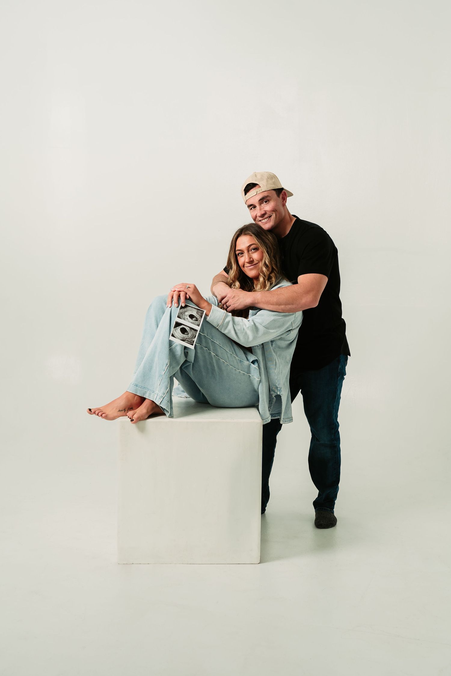 Couple in black and light blue outfits pose playfully against white backdrop in four connected studio photos.