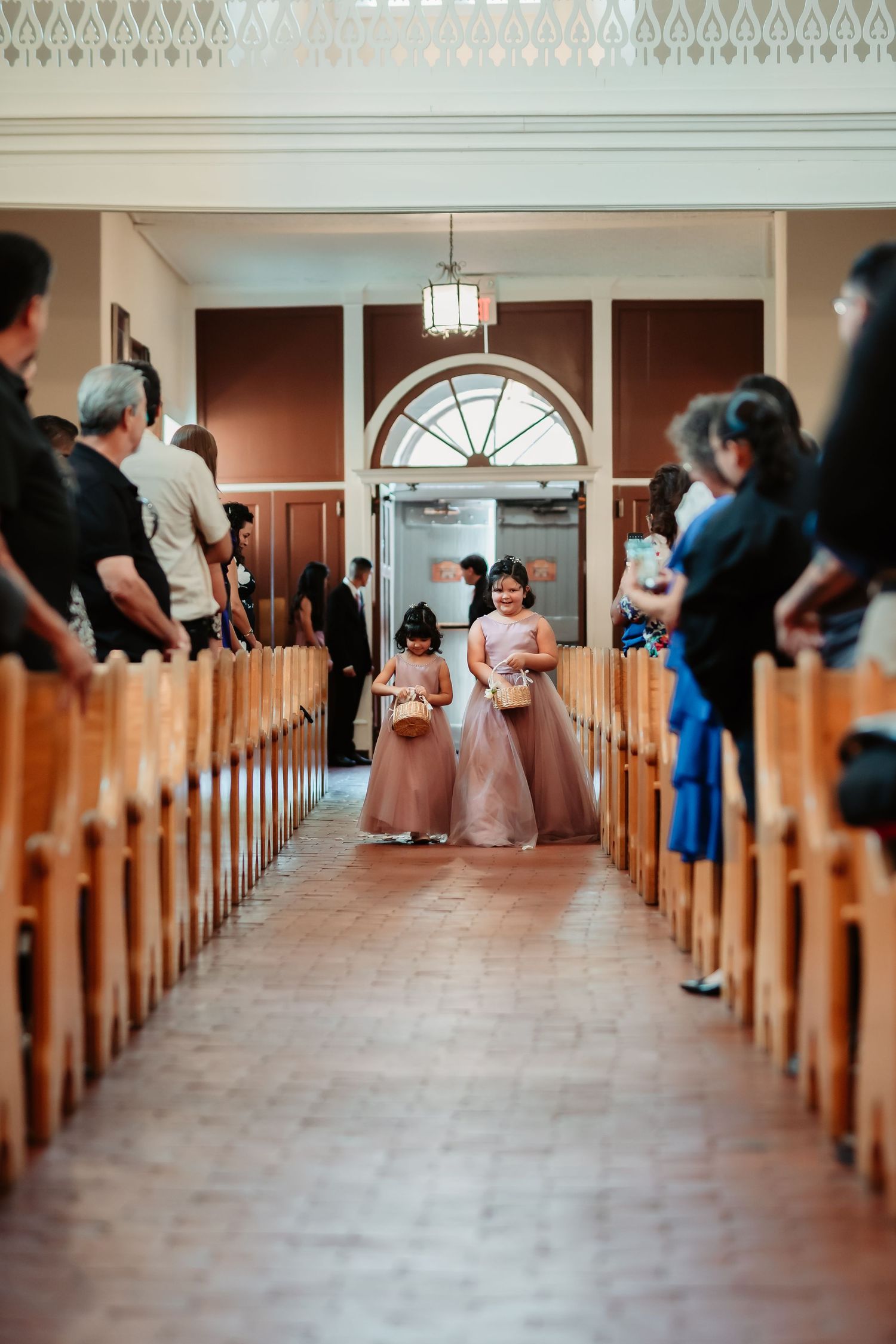 Wedding guests walk down the church aisle with terracotta flooring and wooden pews.