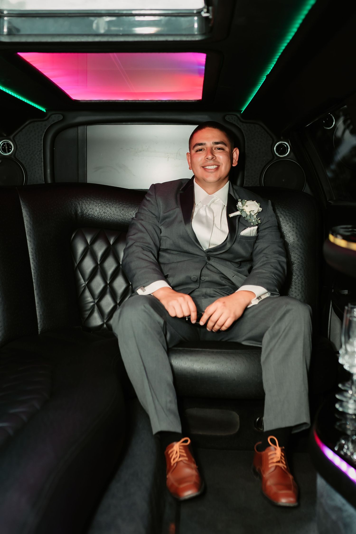 A person in formal attire sits in a luxury car interior with neon lighting and leather seating.