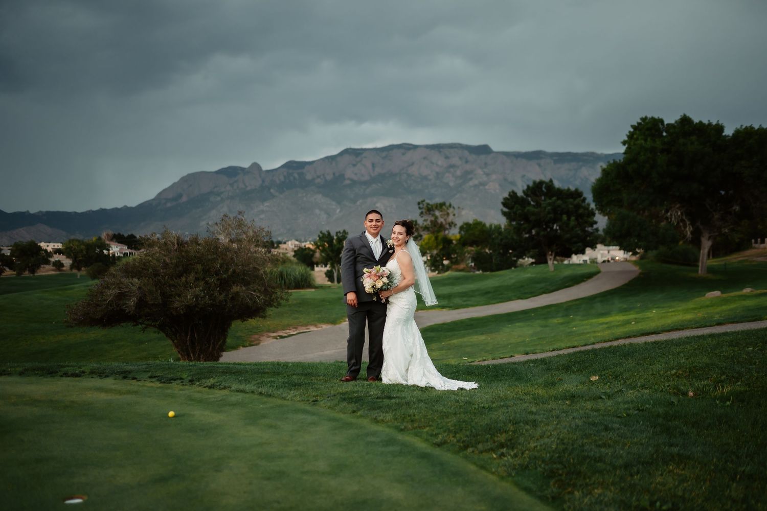Panoramic view of wedding couple on golf course with dramatic mountain landscape.