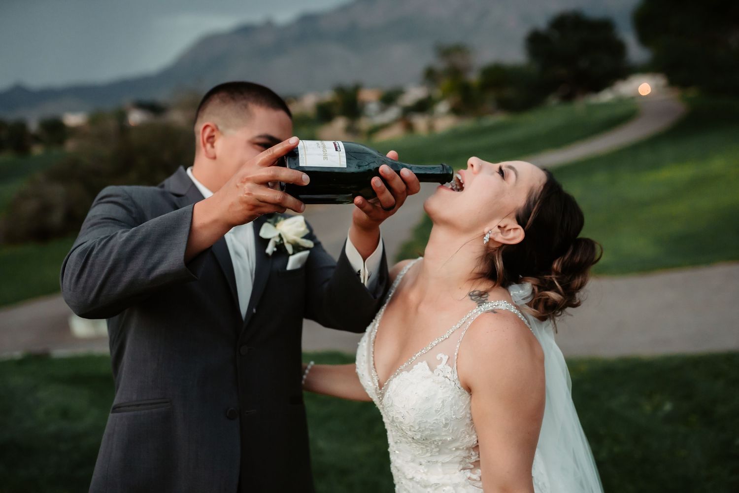 Newlyweds enjoying champagne toast on golf course with mountain views.