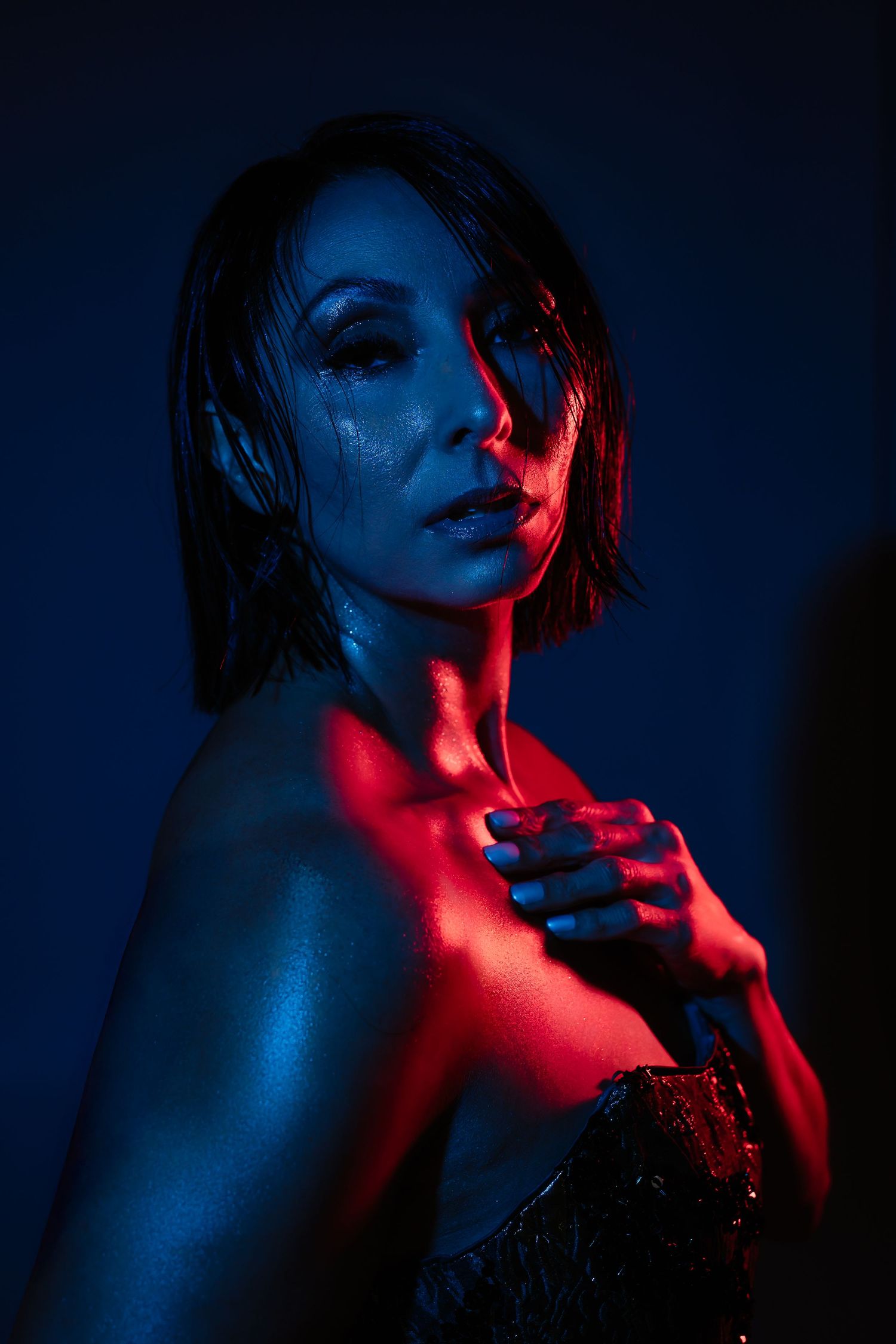 Dramatic portrait with red and blue lighting creating moody contrast against dark background.