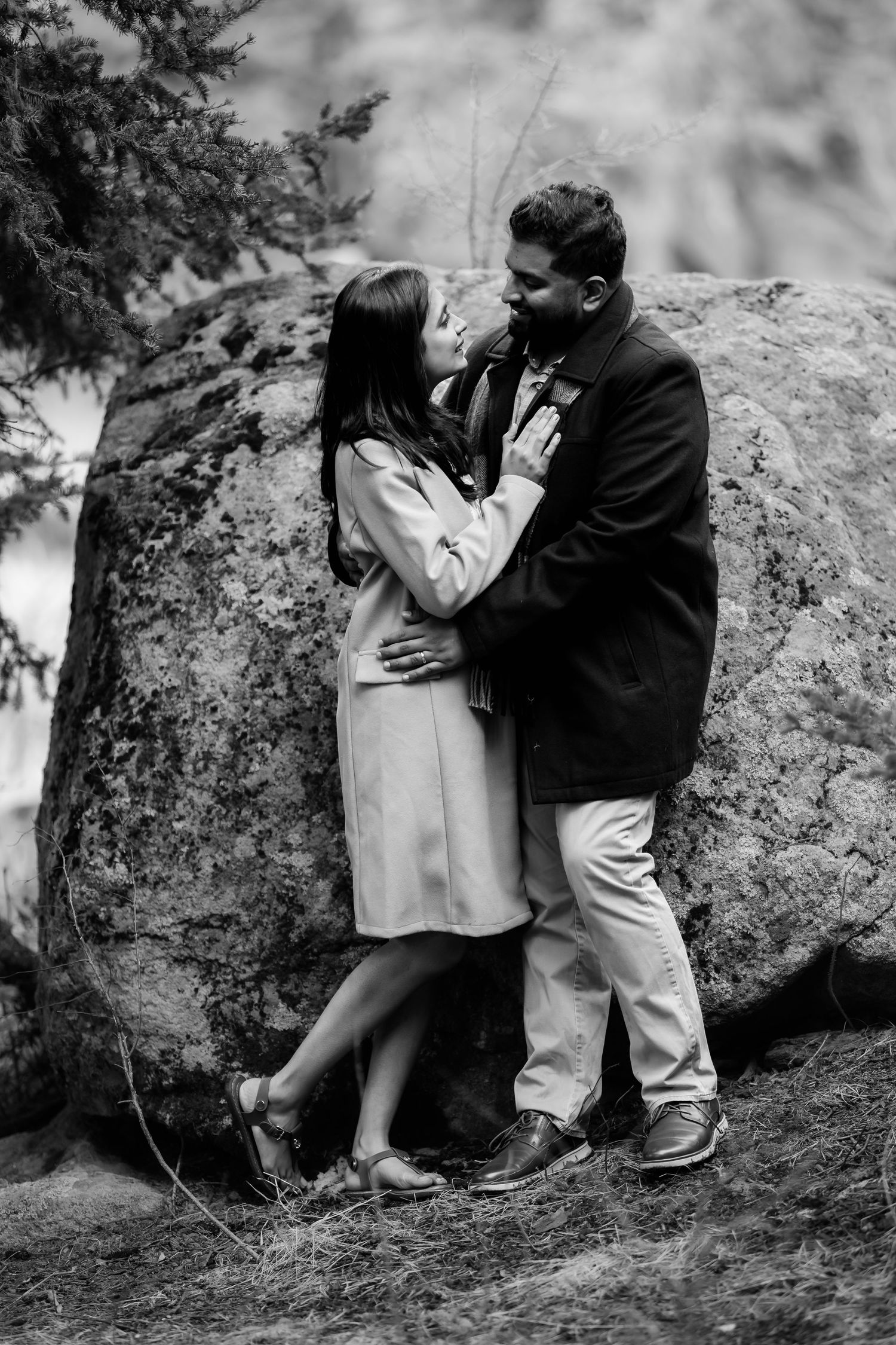 A romantic couple shares an intimate moment against a large boulder in a natural outdoor setting.