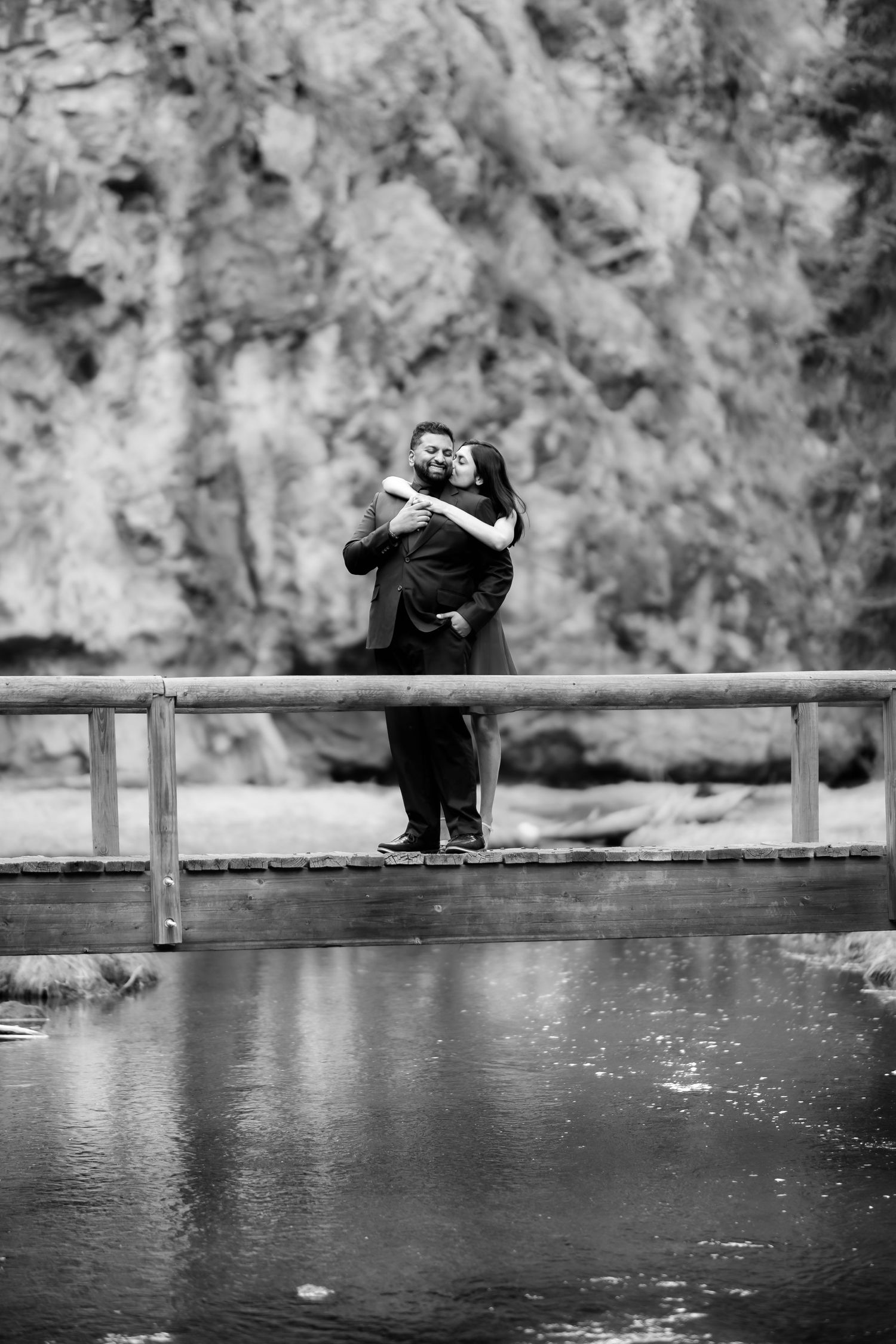 A couple shares an intimate embrace while standing on a wooden bridge over tranquil waters.