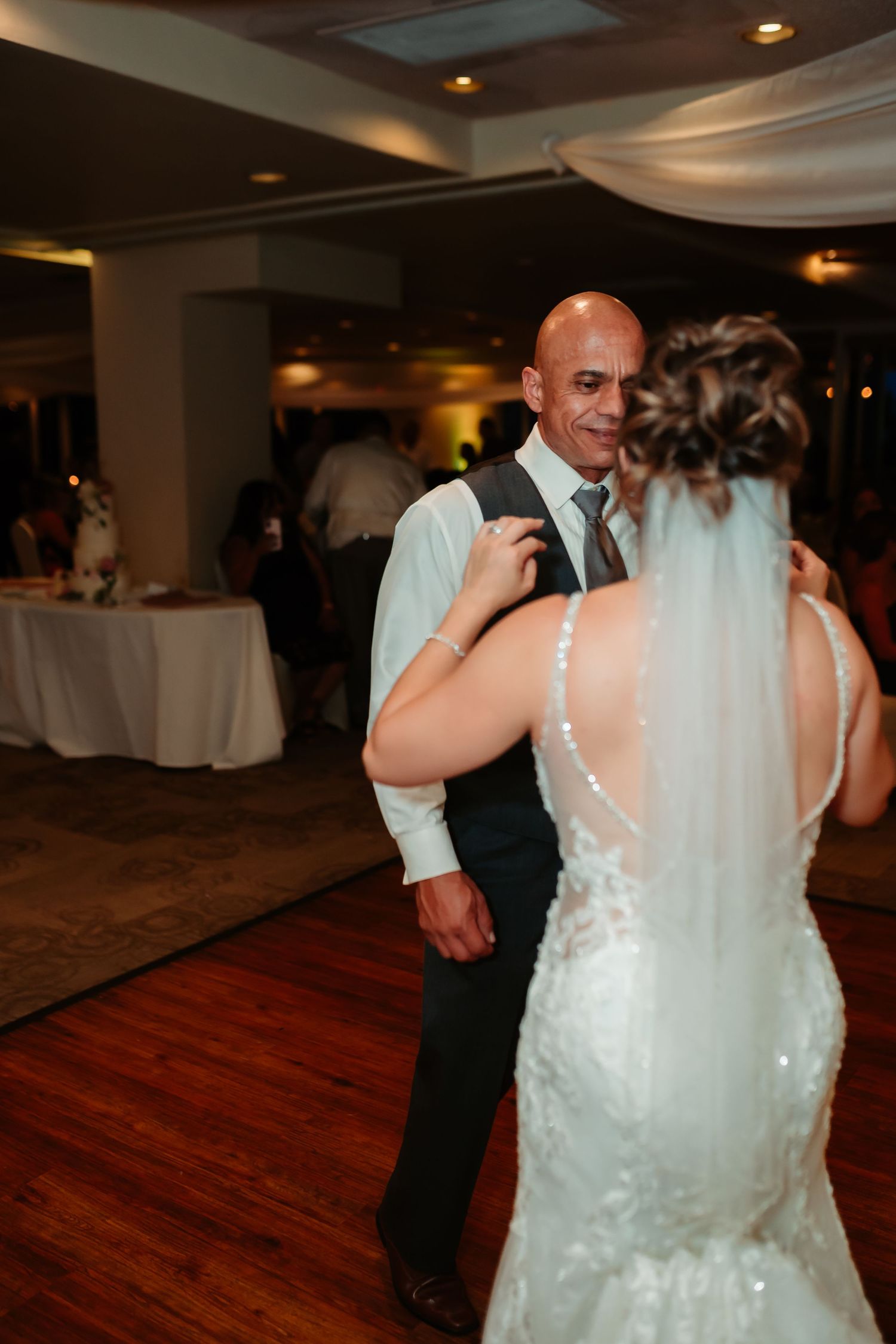 A couple dances together on a wooden dance floor at their wedding reception with ambient lighting and decor.