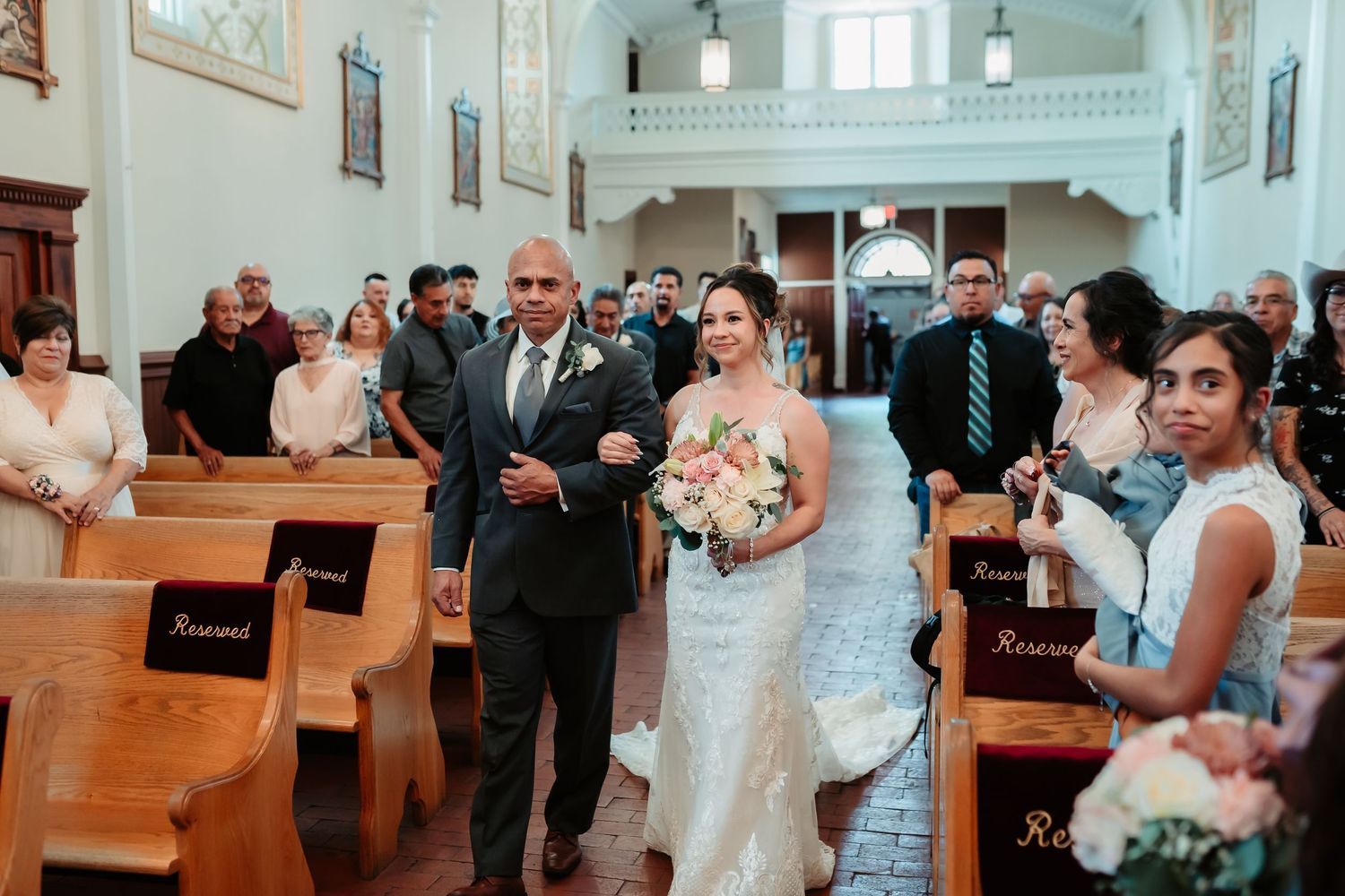 Wedding guests seated in white wooden pews inside a bright traditional church sanctuary.