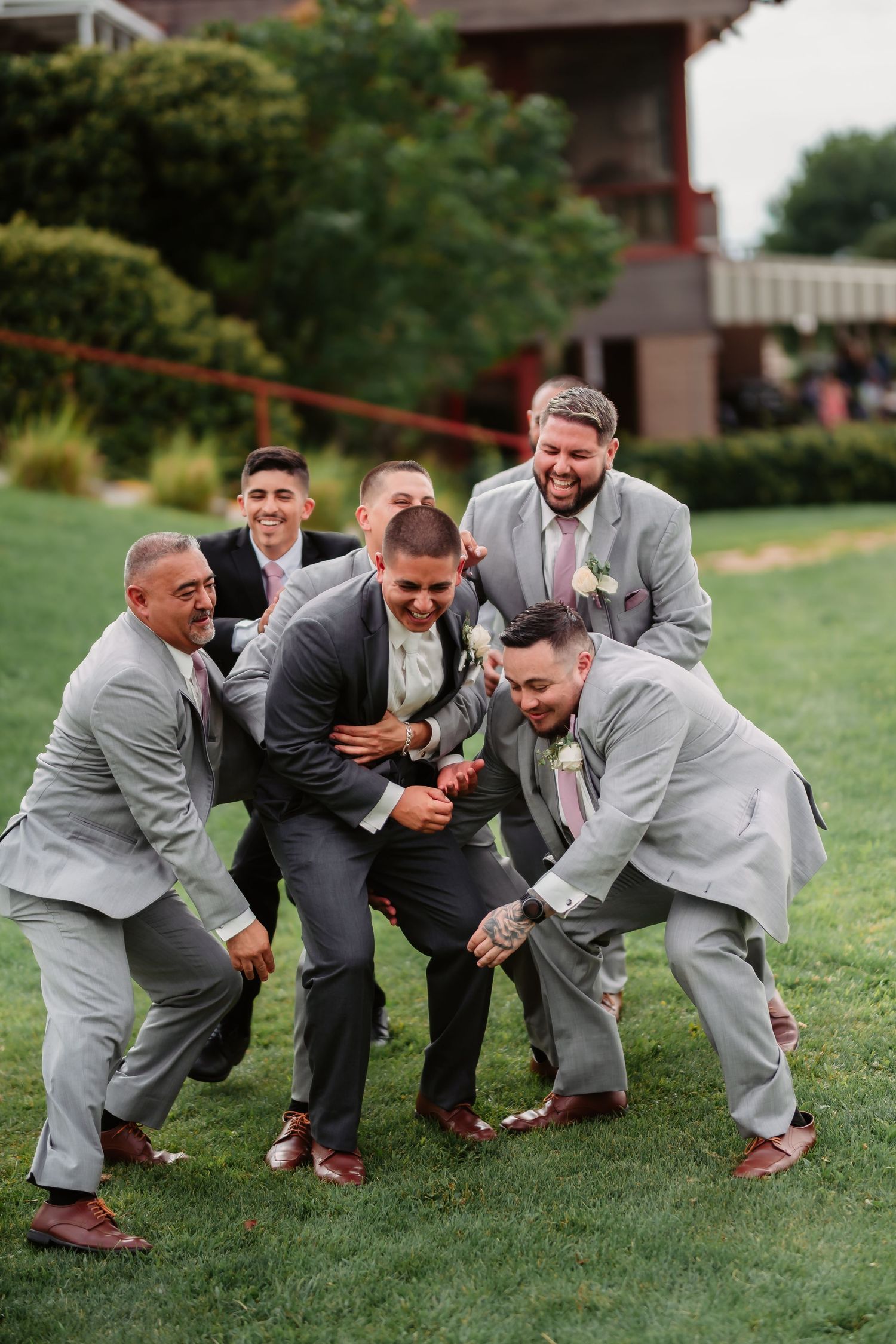 A sequence of five photos capturing groomsmen in suits playfully crouching on green grass during a wedding.