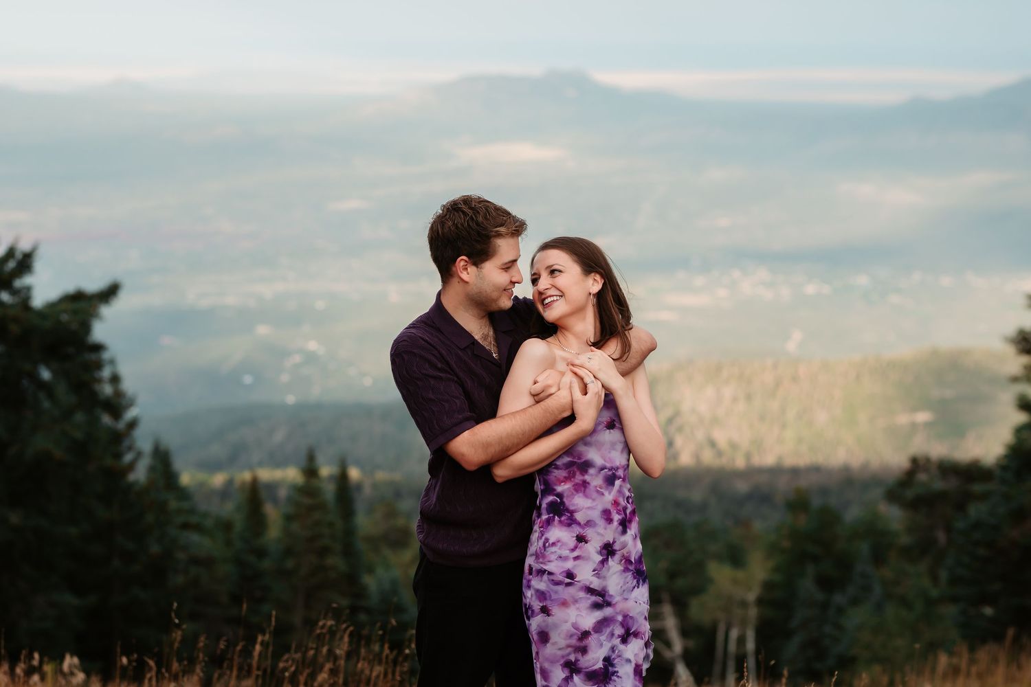 A romantic couple enjoying a tender moment in a mountain meadow at dusk.