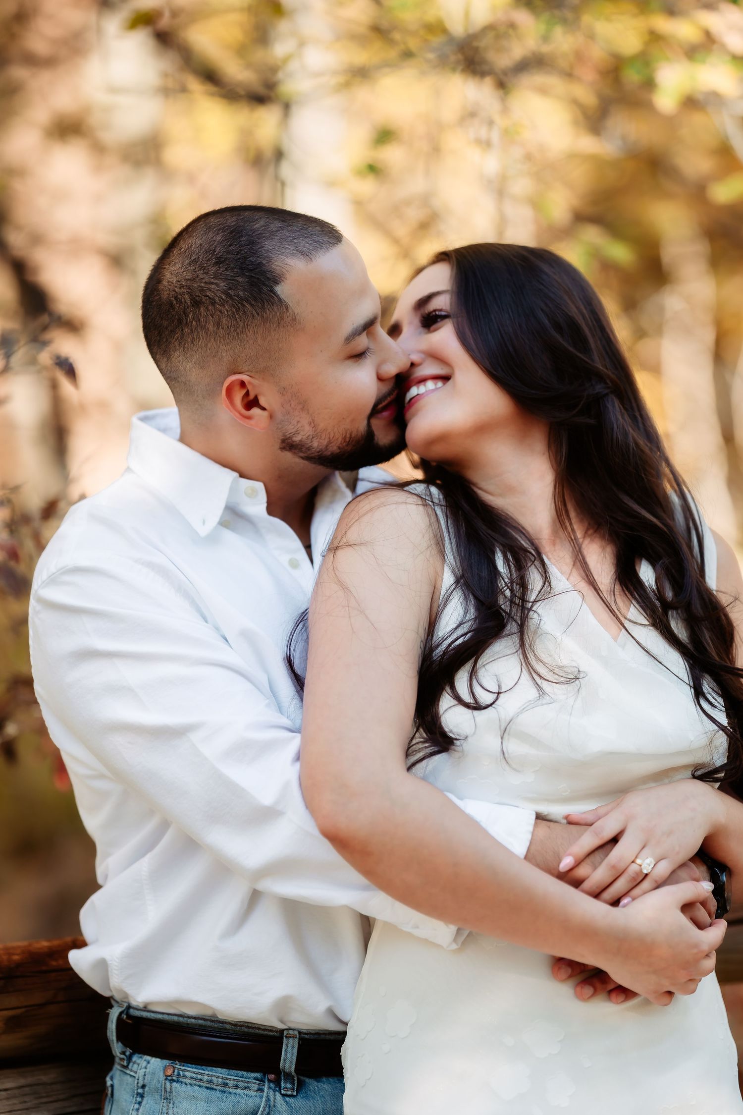 A romantic couple embraces and shares tender kisses in a series of outdoor engagement photos with autumn foliage.