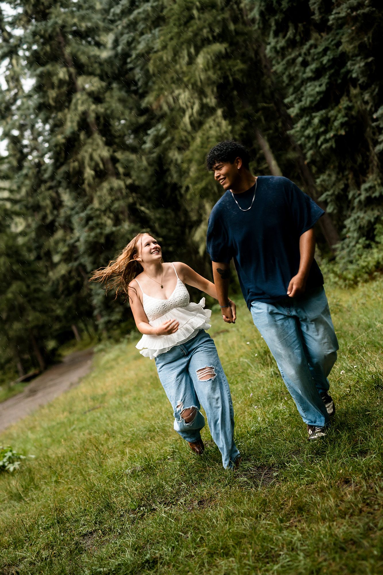 Young interracial couple holding hands and running through a lush green forest park, laughing joyfully.