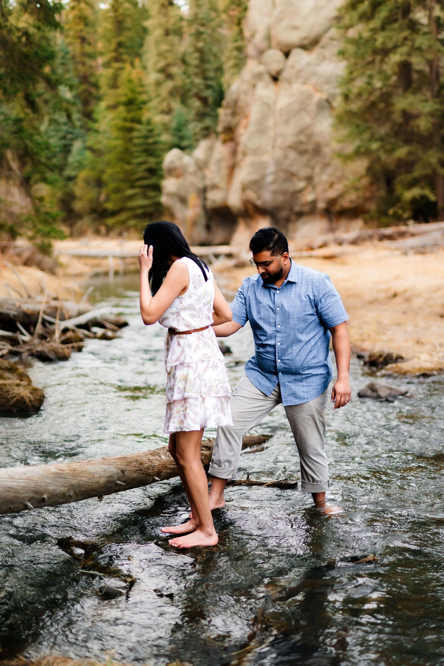 A couple explores a mountain stream together, carefully stepping on rocks.