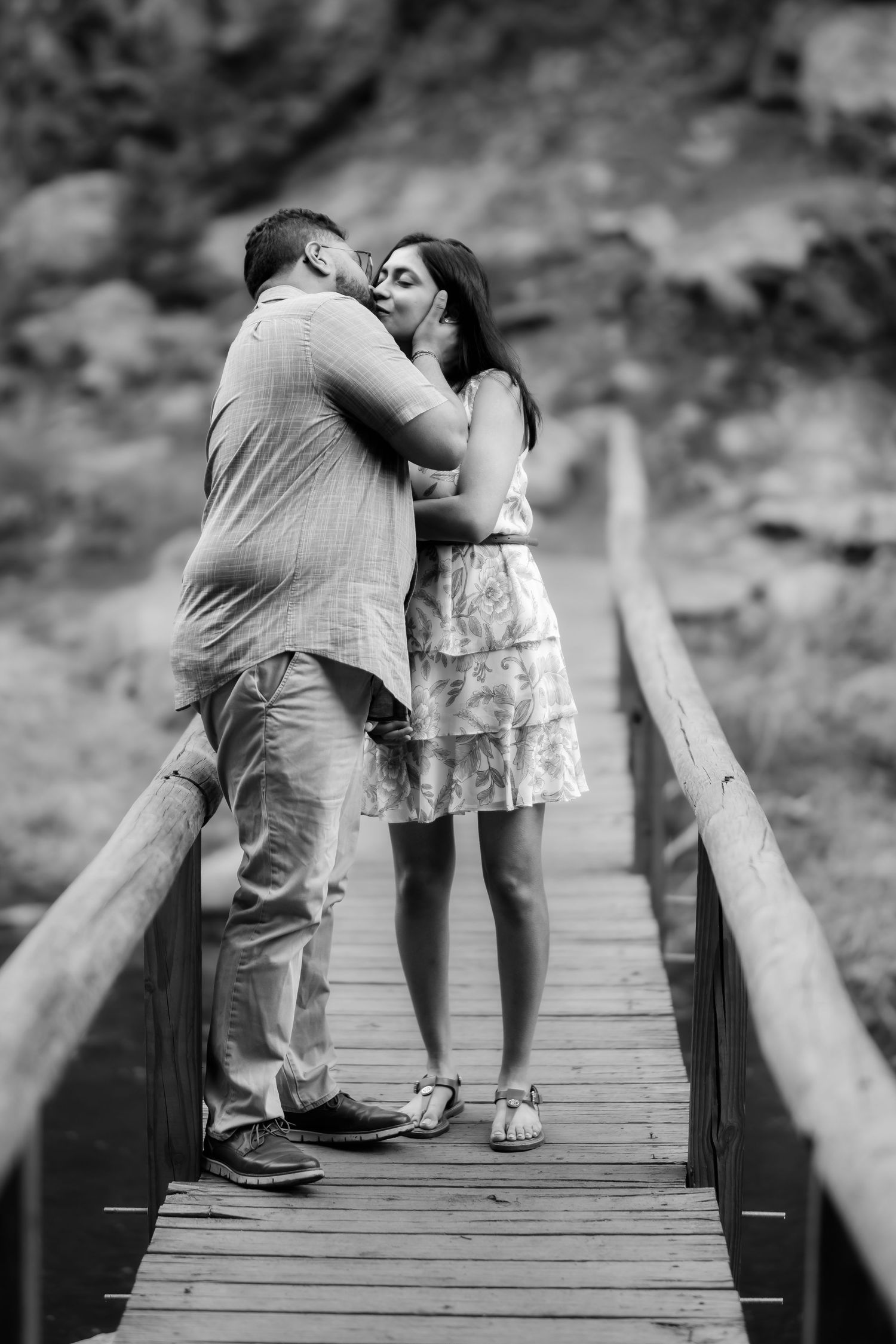 Intimate black and white moment captured of a couple kissing on a wooden footbridge.