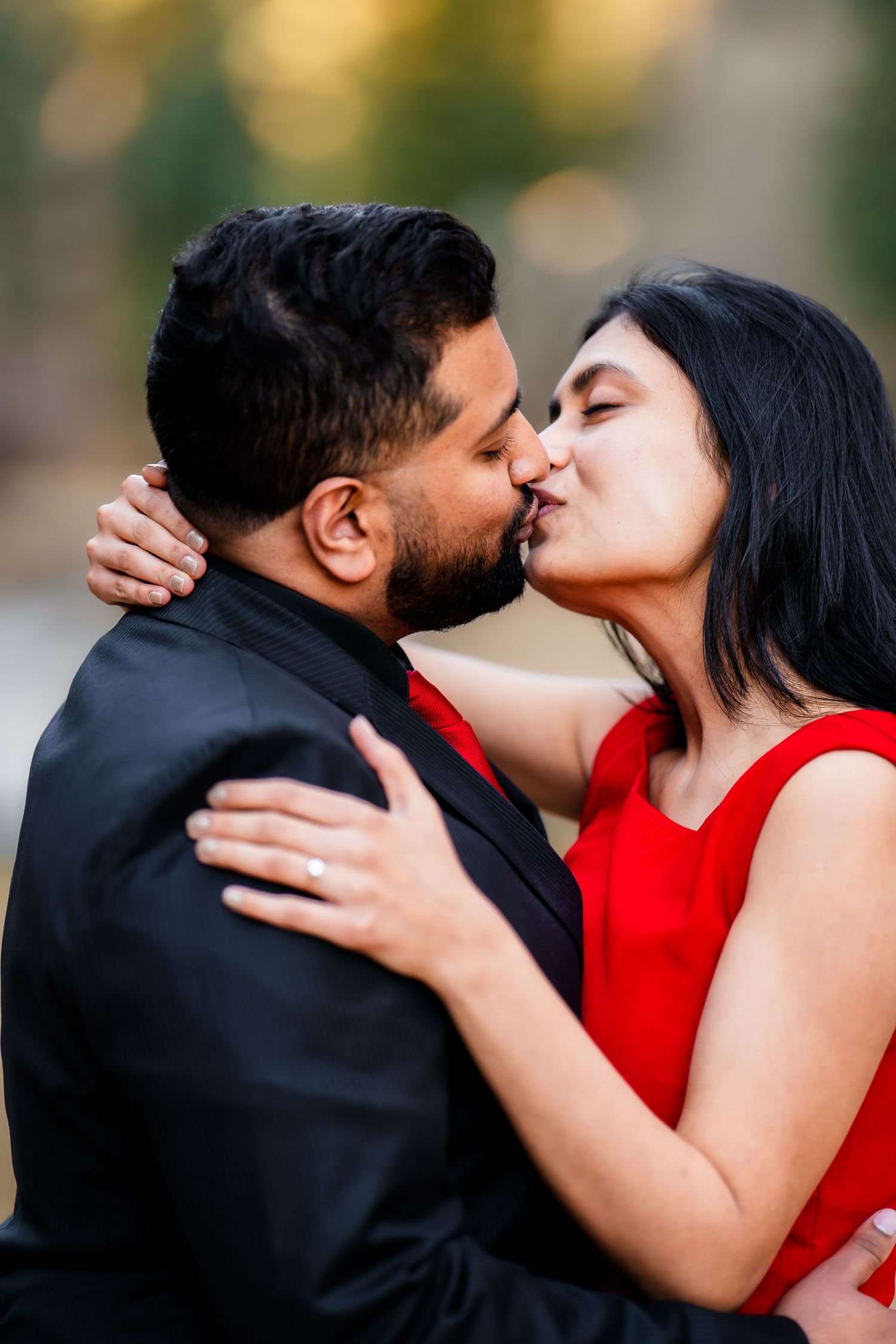 Romantic couple in formal attire sharing an intimate kiss outdoors with warm bokeh background.