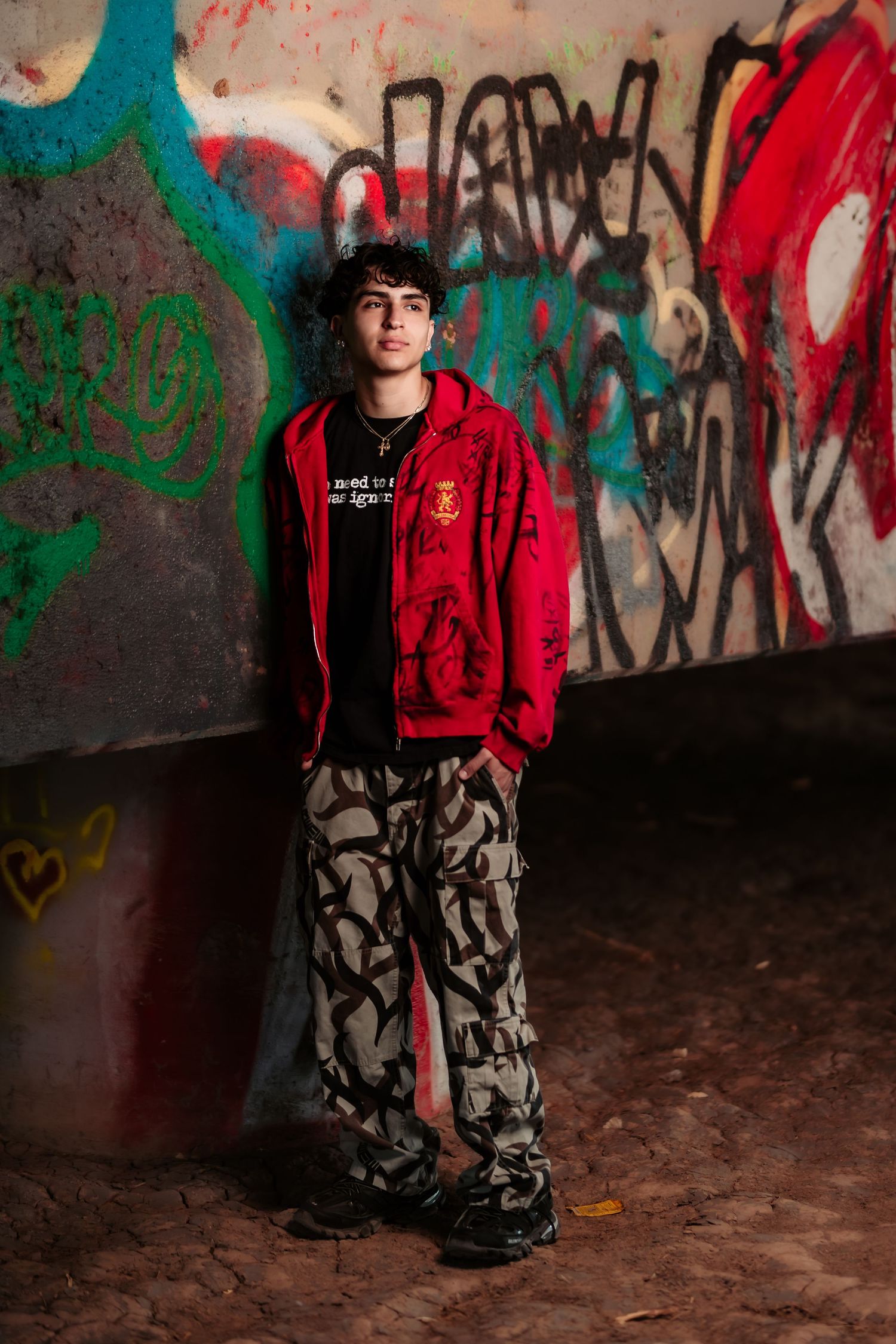 Urban portrait of person in red jacket and camo pants against colorful graffiti wall.