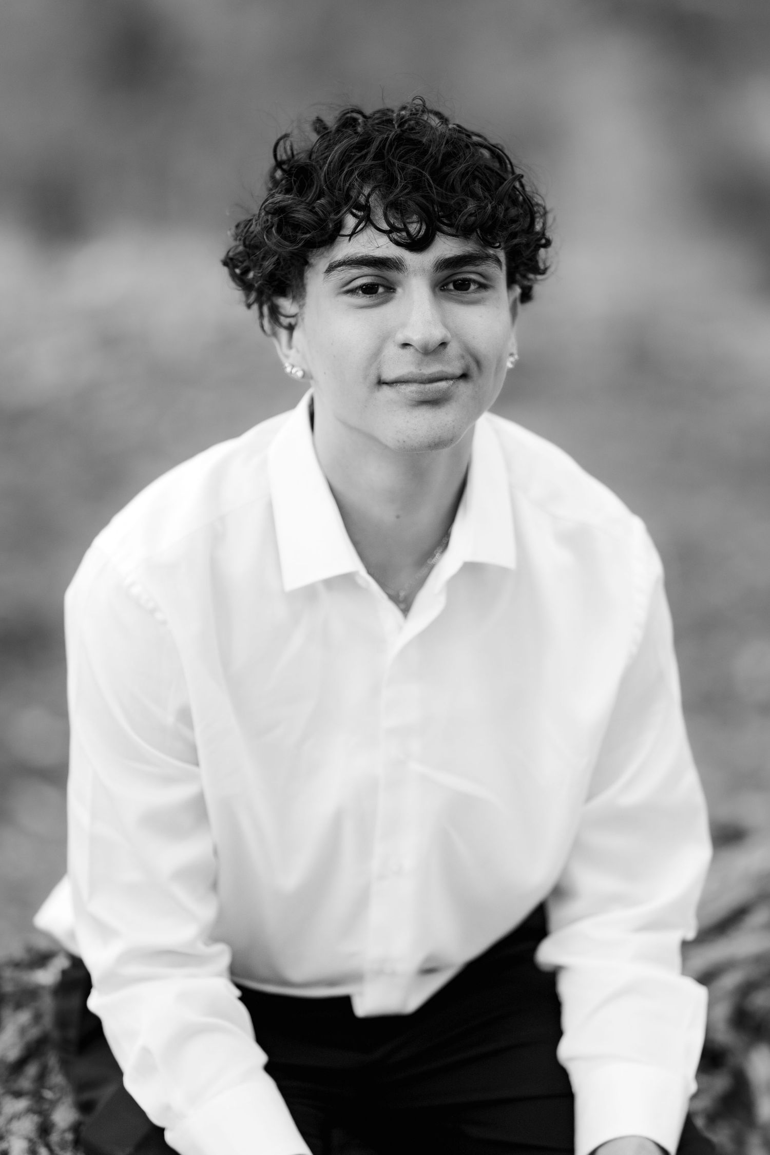 Black and white portrait of someone wearing a white button-down shirt and dark pants with curly hair and an earring.