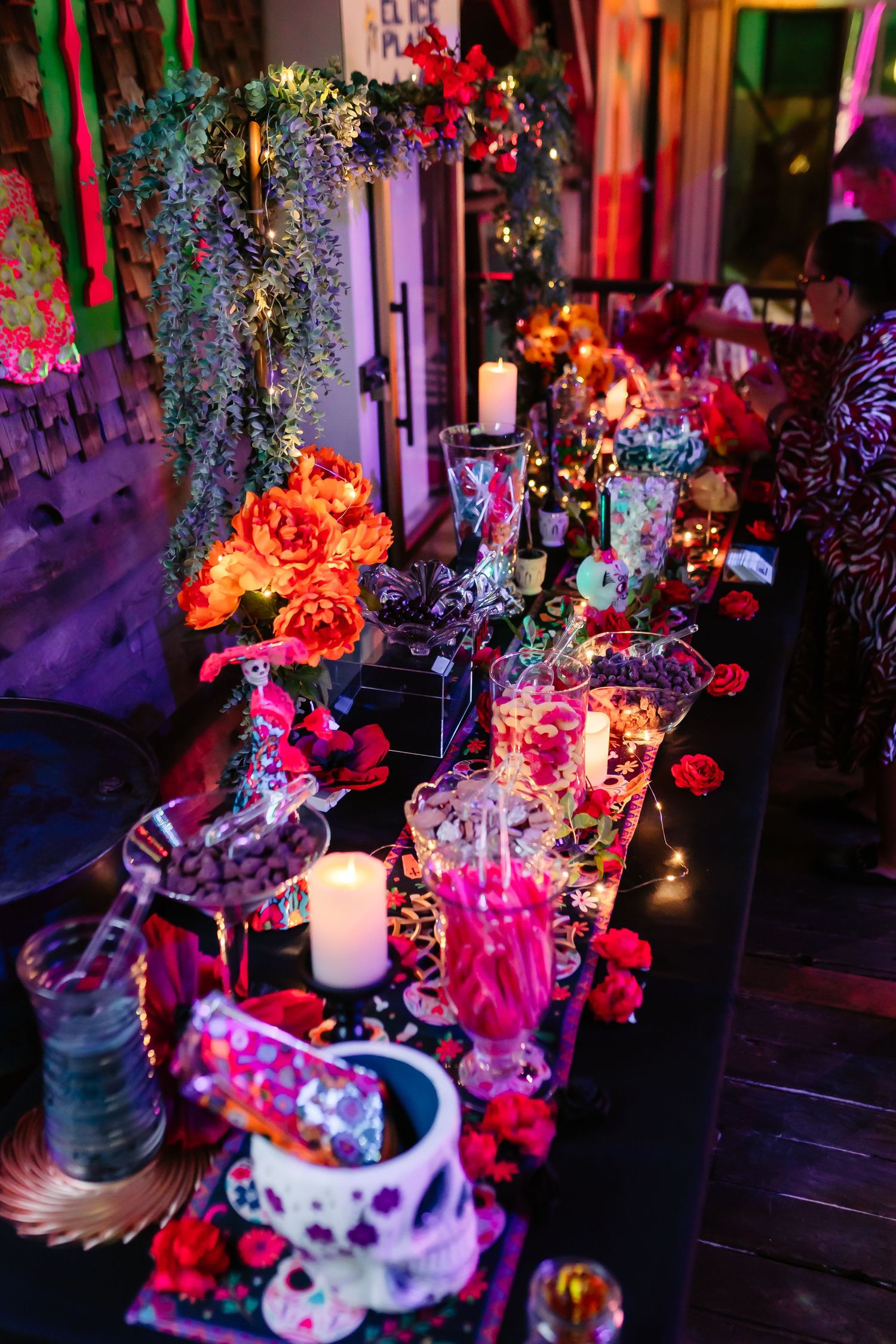 Colorful floral arrangements with glowing candles and teacups create a whimsical Alice in Wonderland themed party setting.