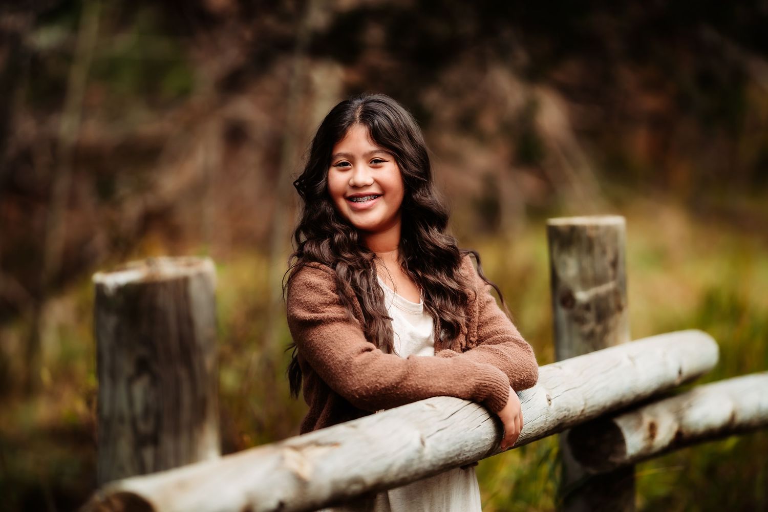 Person in brown leather jacket leans against rustic wooden fence rail in outdoor autumn setting.