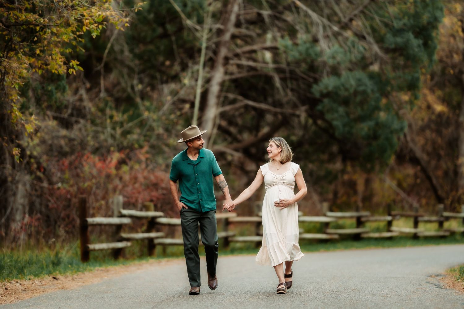 A couple strolls together on a tree-lined path during autumn with colorful fall foliage in the background.
