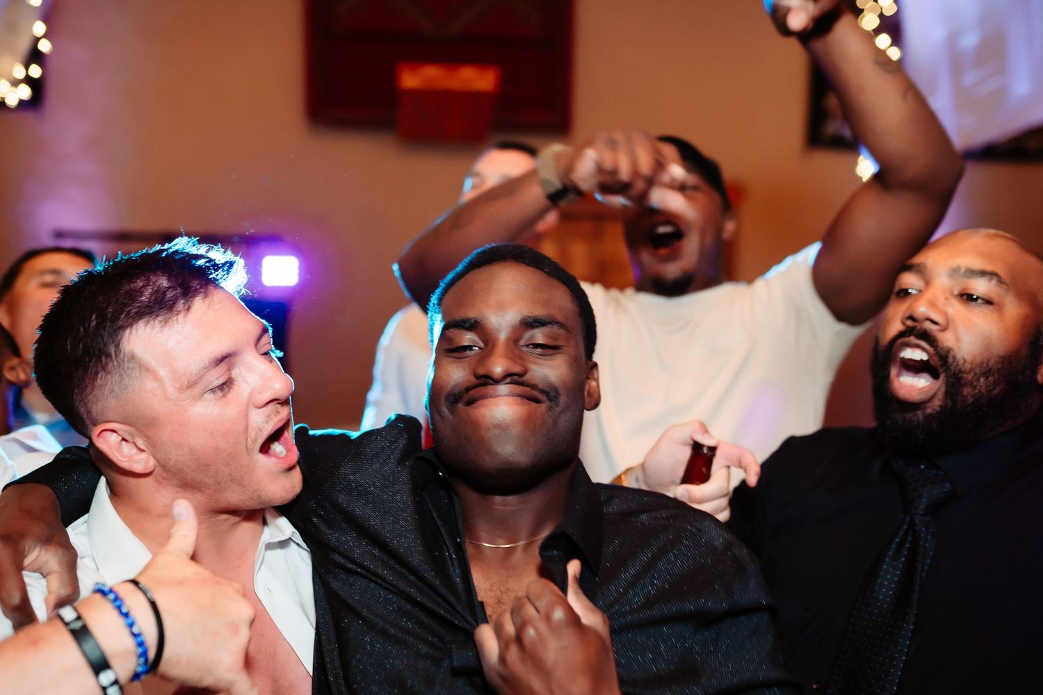 A group of people laughing together with their heads tilted back in a joyful moment at an indoor gathering.