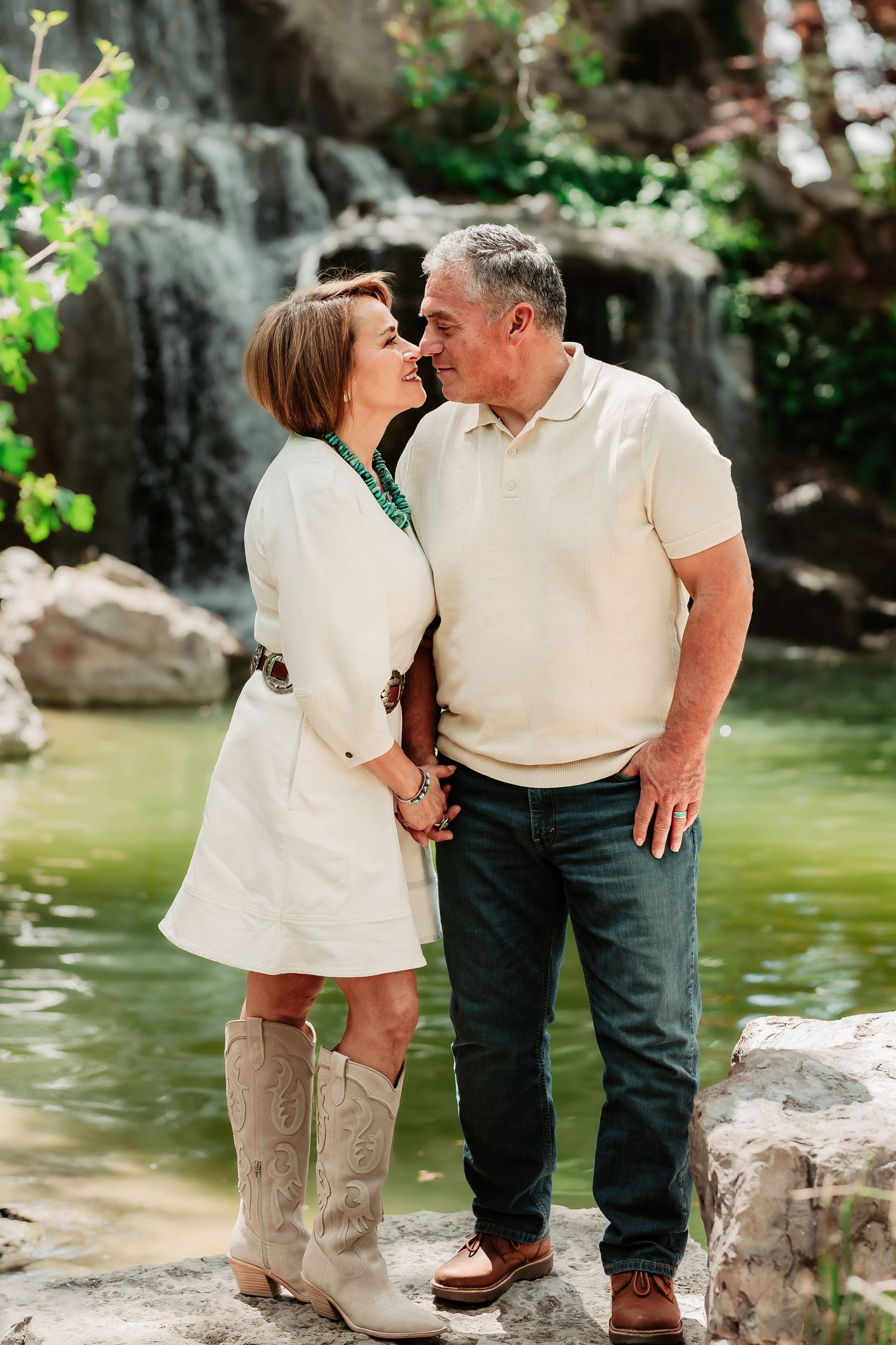 A romantic couple shares tender moments by a pond in a natural outdoor setting.