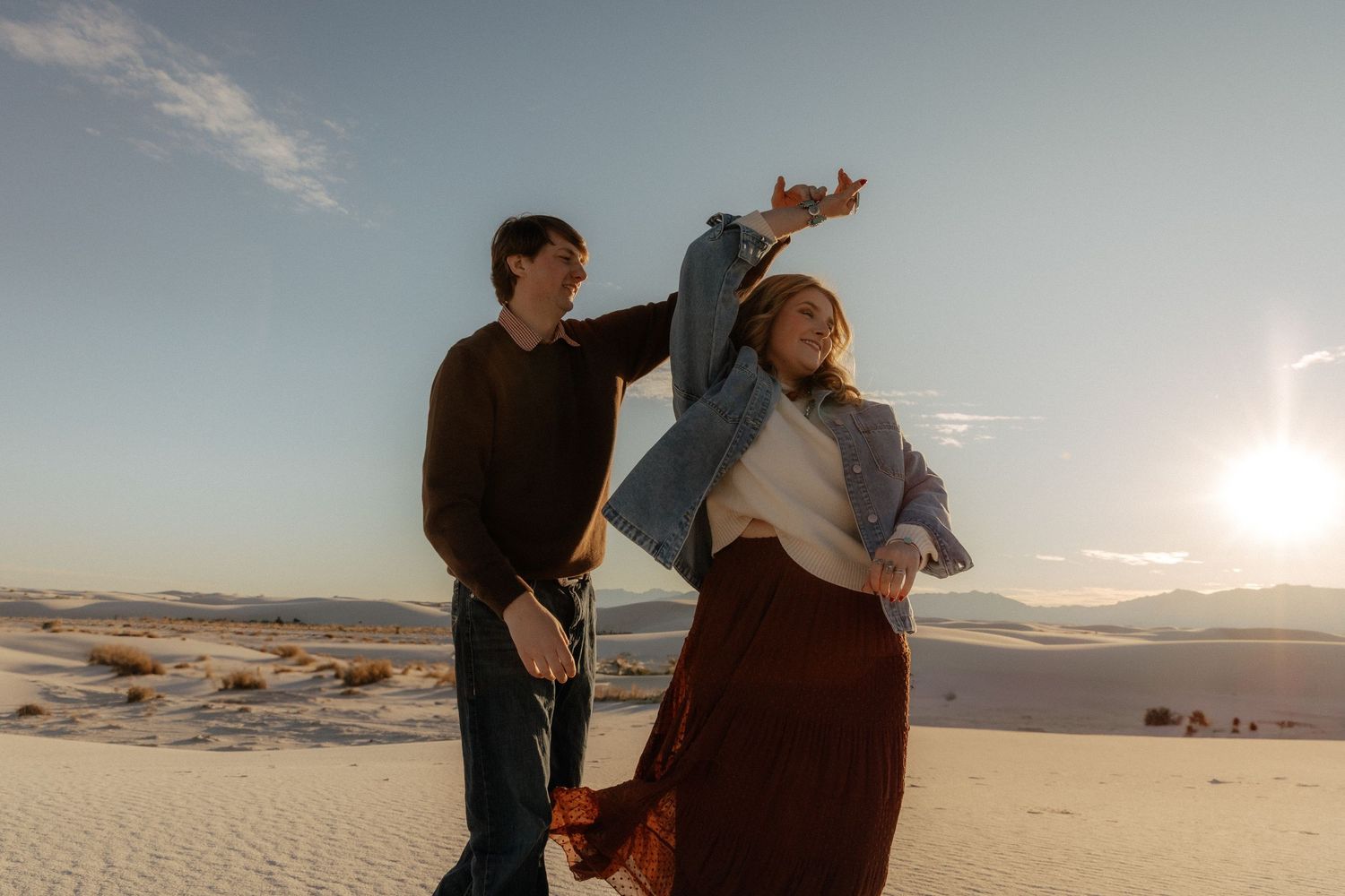 Couple dancing joyfully on white sand dunes at sunset in White Sands National Park, New Mexico.