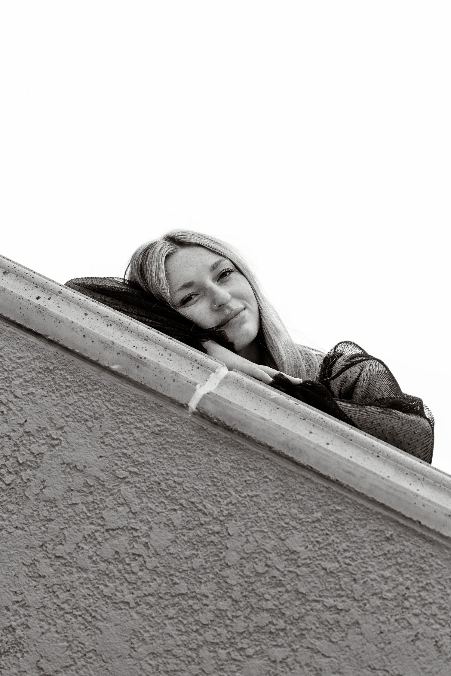 Black and white photo of blonde woman peeking over a concrete ledge.