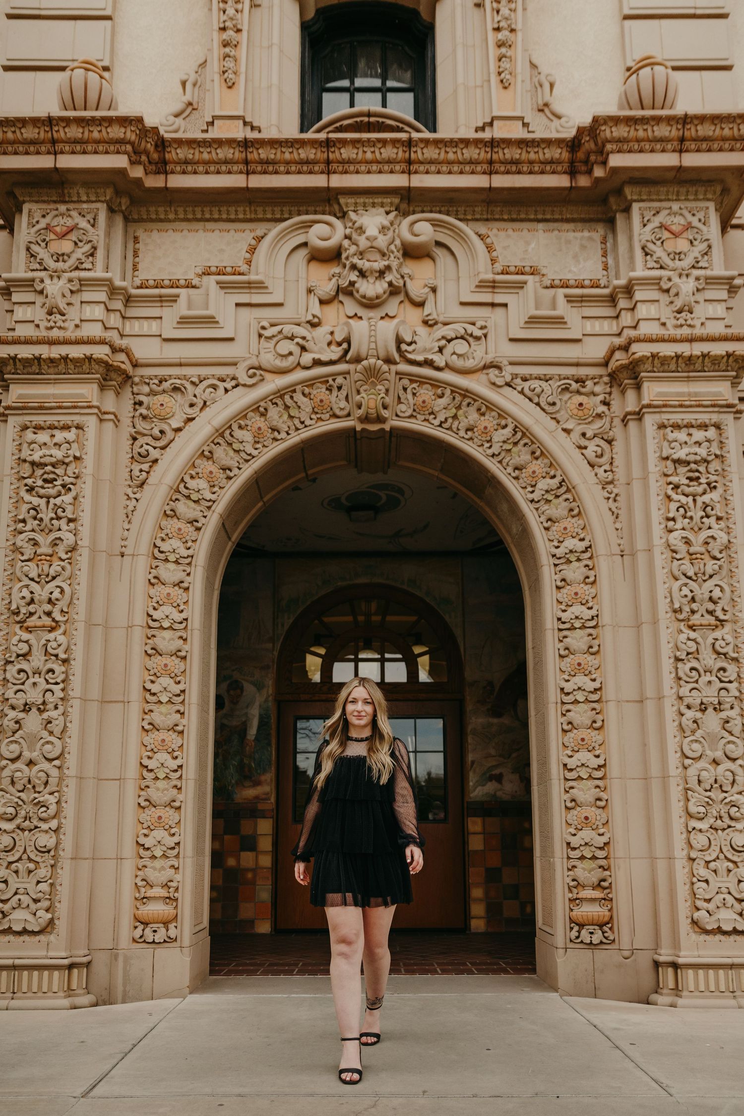 Woman in black dress walking through ornate decorative archway of historic building.