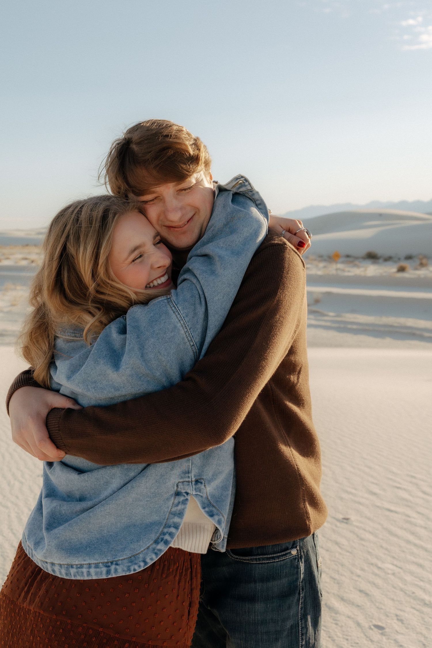 Couple embracing warmly on white sand dunes at sunset in a desert landscape.