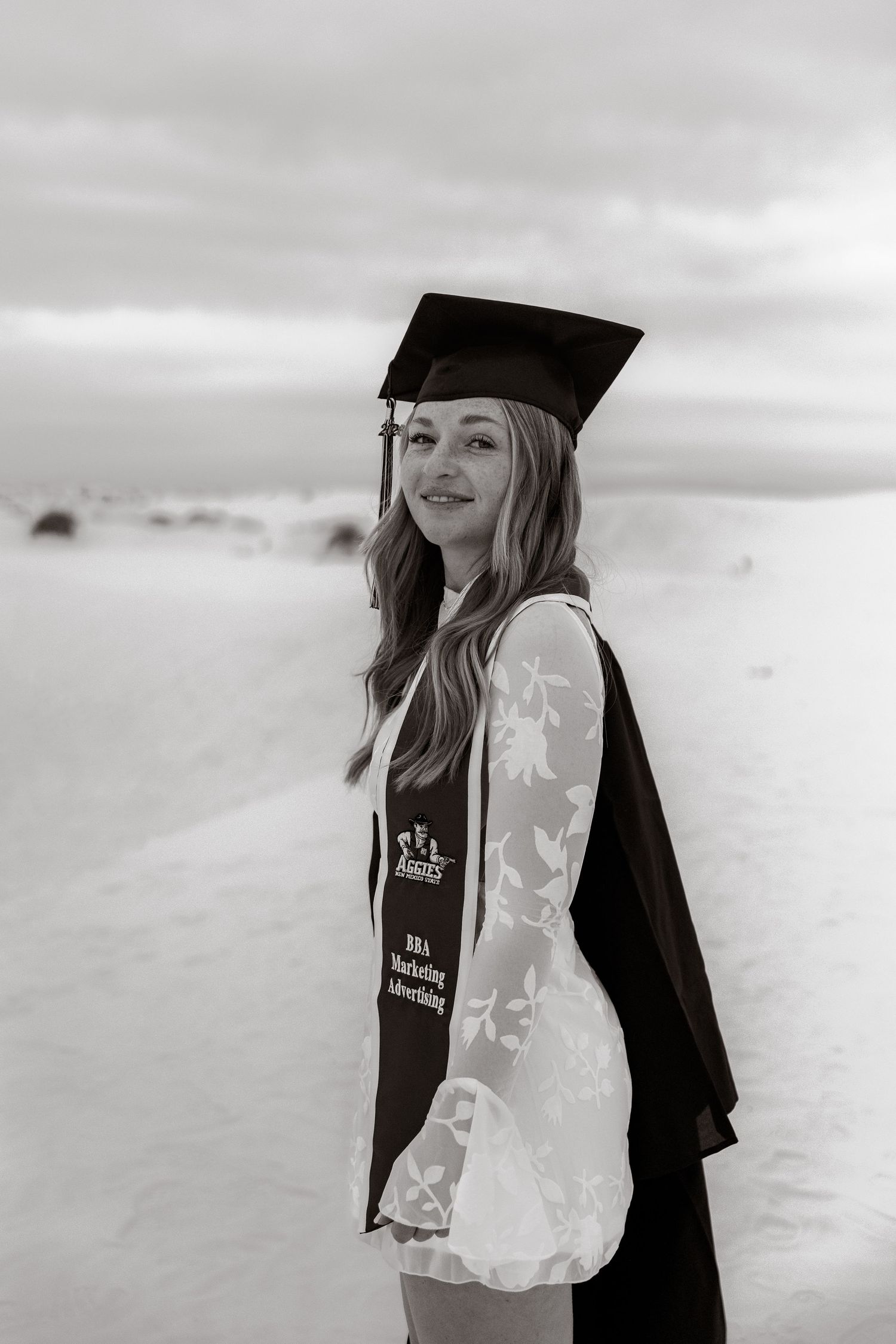 Black and white portrait of graduate in cap and gown with BBA Marketing Advertising stole.
