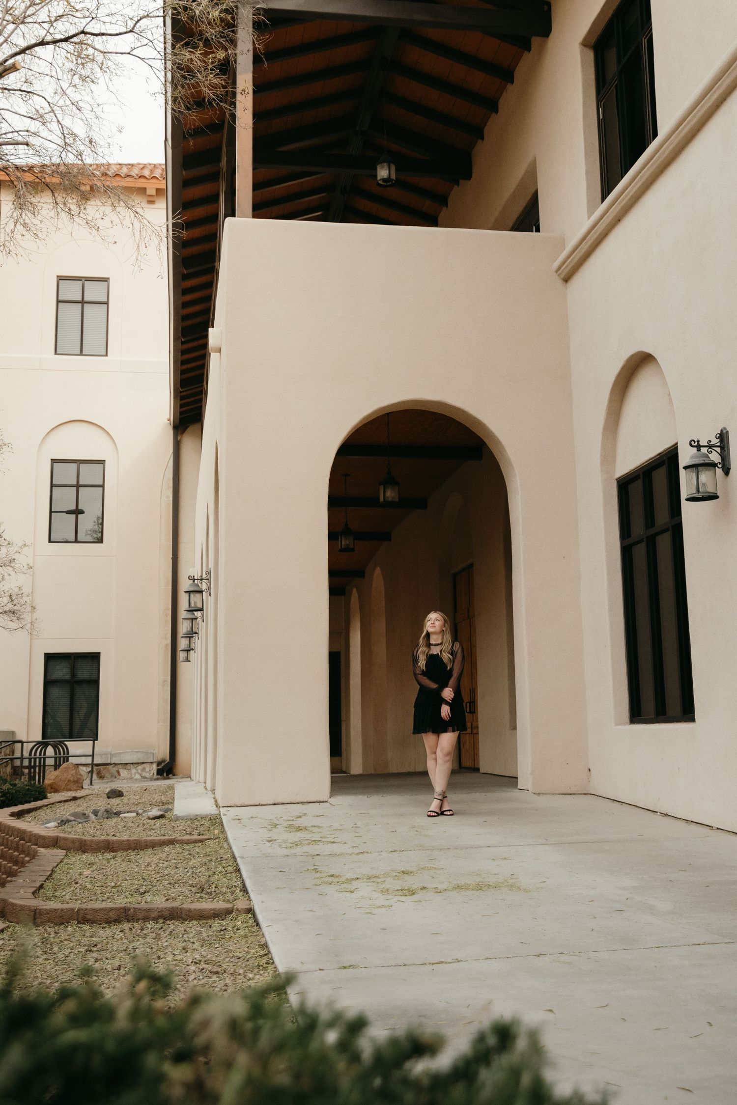 Blonde woman in black dress walking through arched entryway of university building.