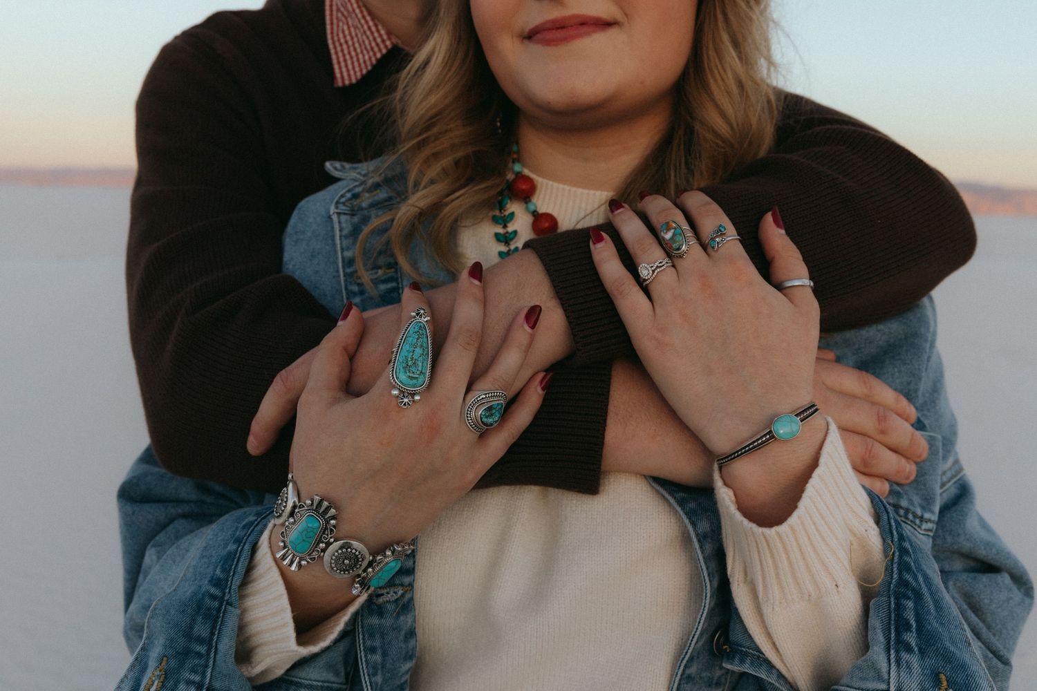 Close-up of a couple embracing, showcasing turquoise and silver rings and bracelets on their hands.