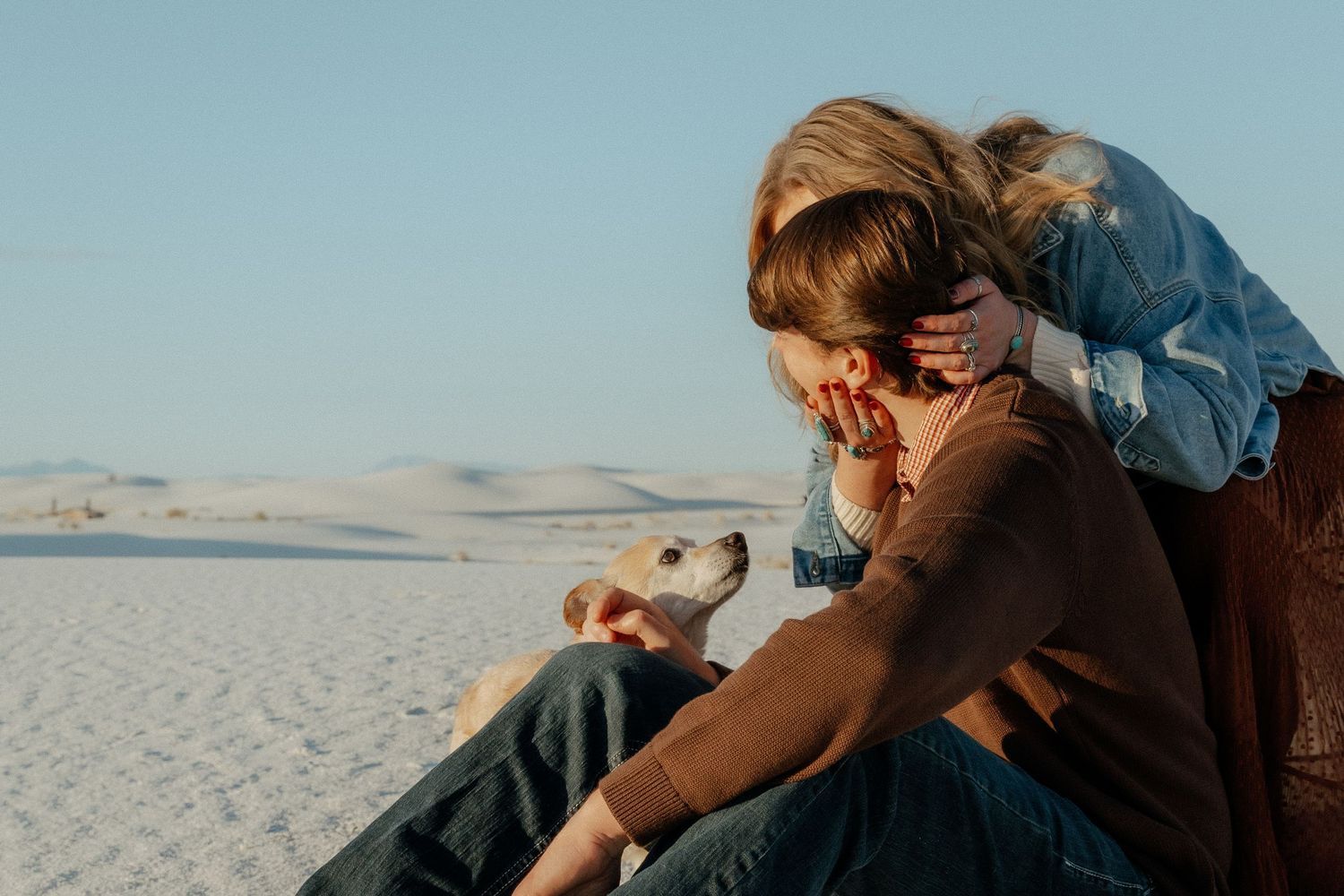 Couple sitting on white sand dunes with their dog at golden hour.