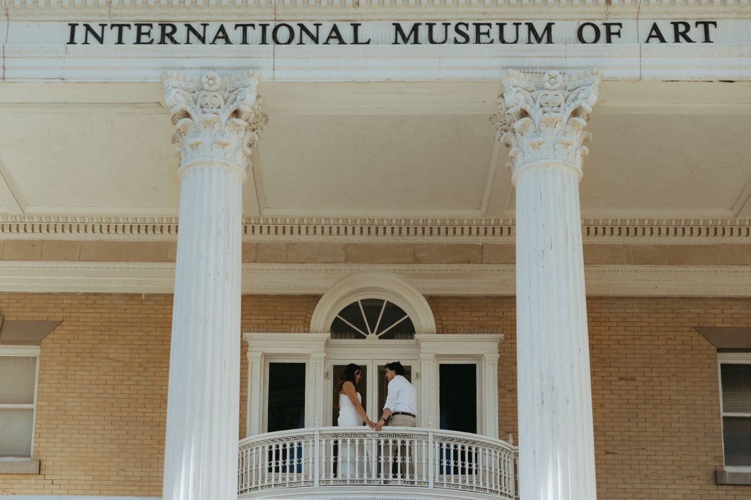 Couple standing on balcony of International Museum of Art with white columns.
