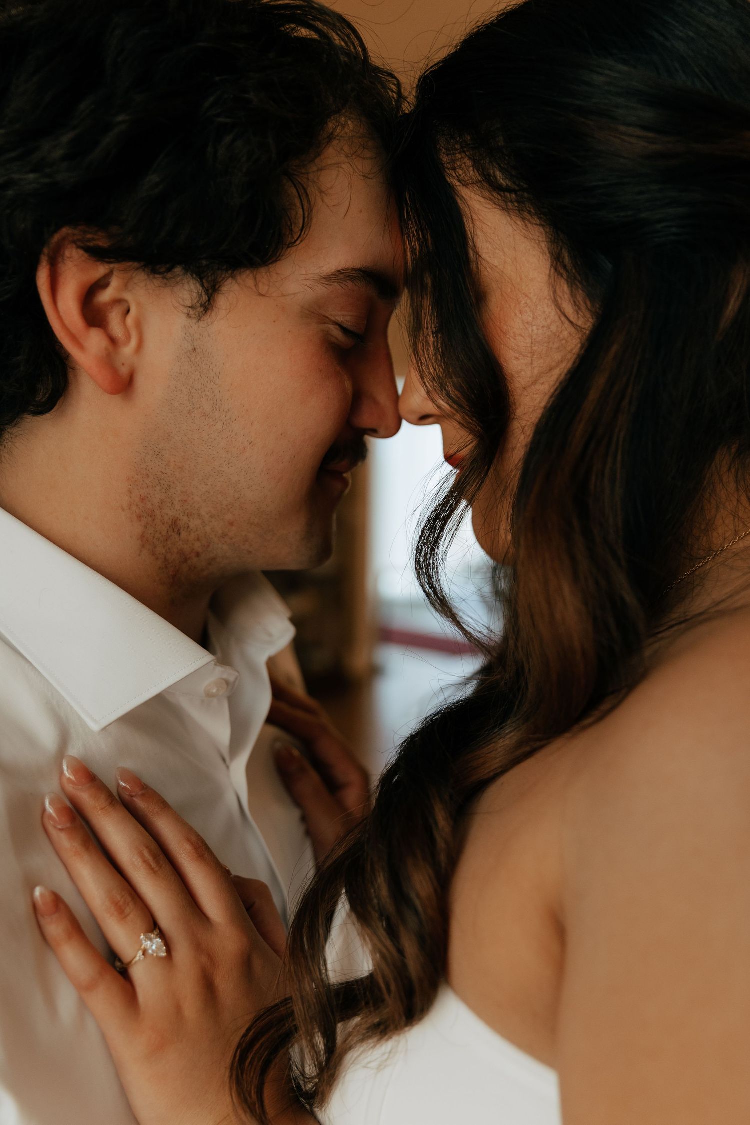 Couple sharing an intimate moment, foreheads touching, bride wearing engagement ring in romantic close-up portrait.