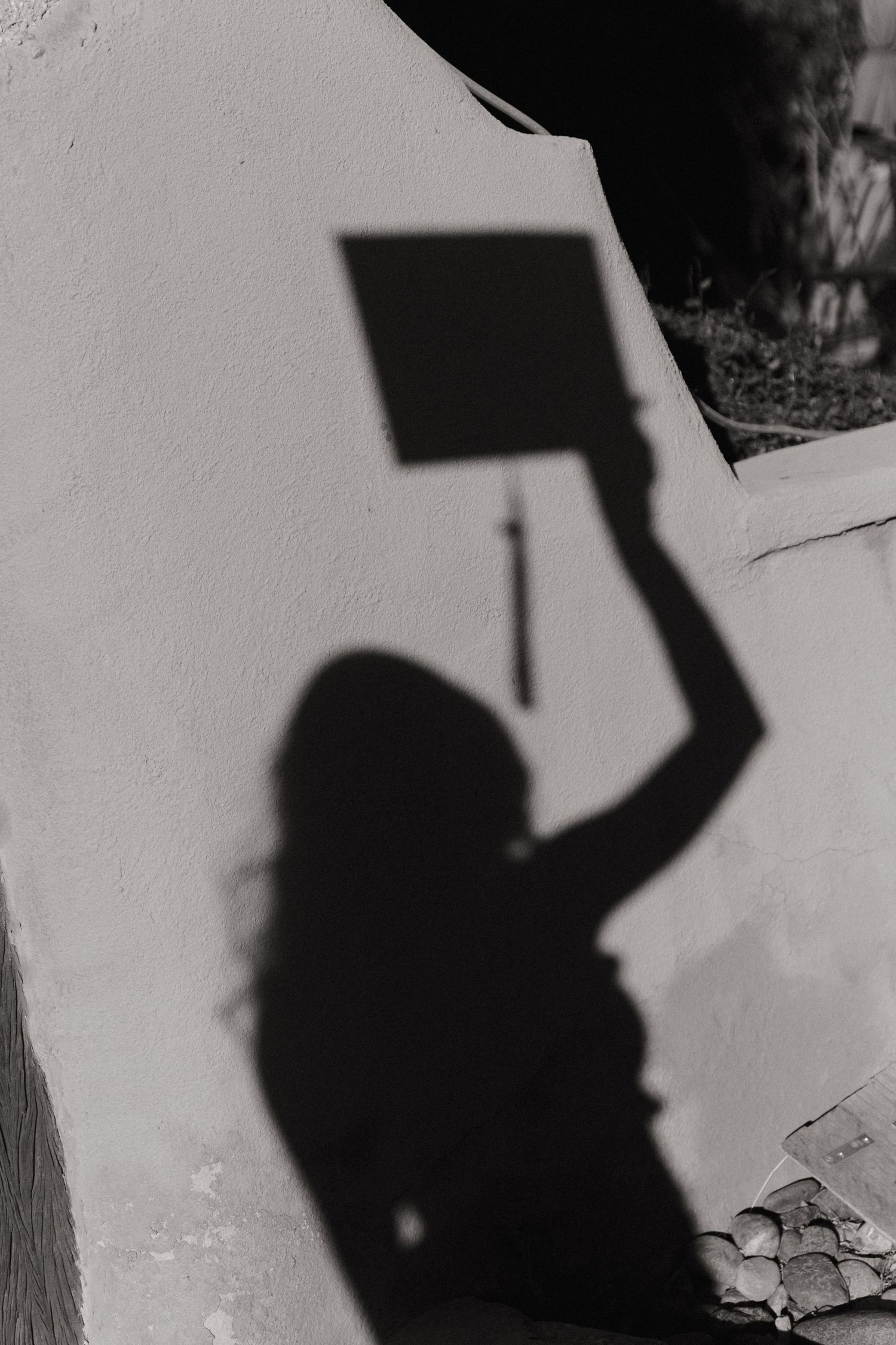 Black and white shadow silhouette of graduate holding cap cast on white wall outdoors.